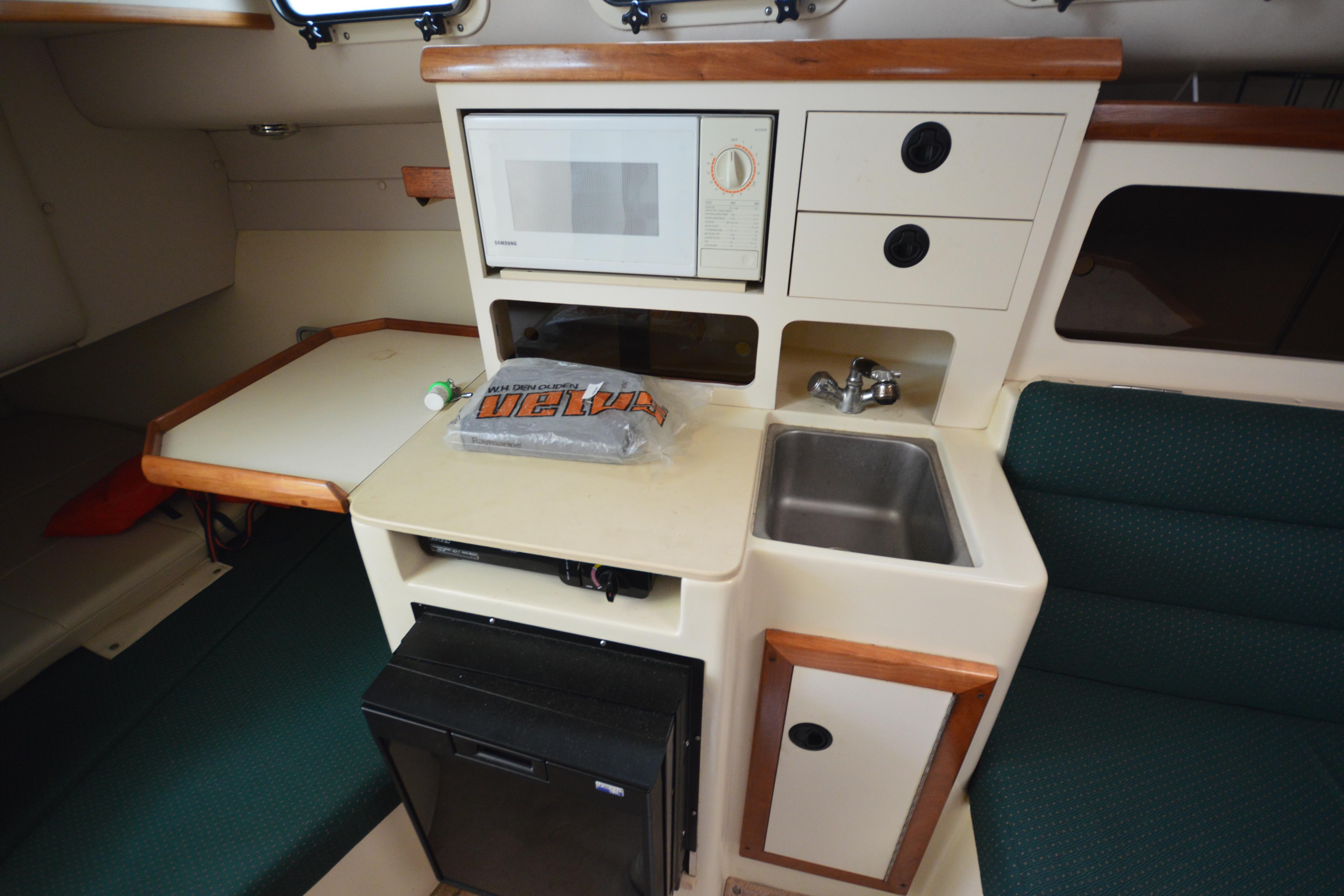 2001 Albin 28 Tournament Express cabin with kitchenette, featuring sink, microwave, and compact fridge.