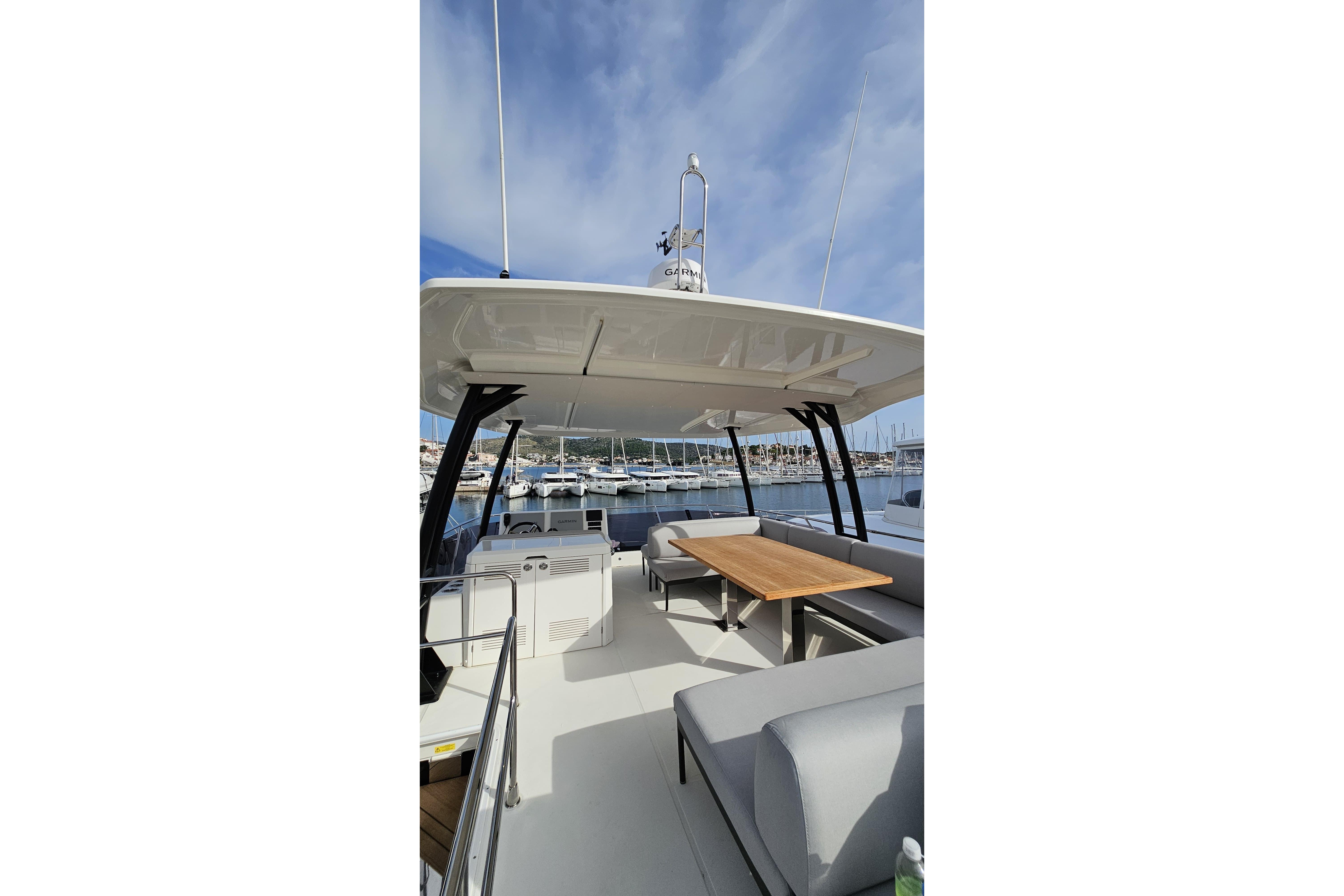 2024 Prestige M48 yacht deck with seating and table, docked at marina under blue sky.