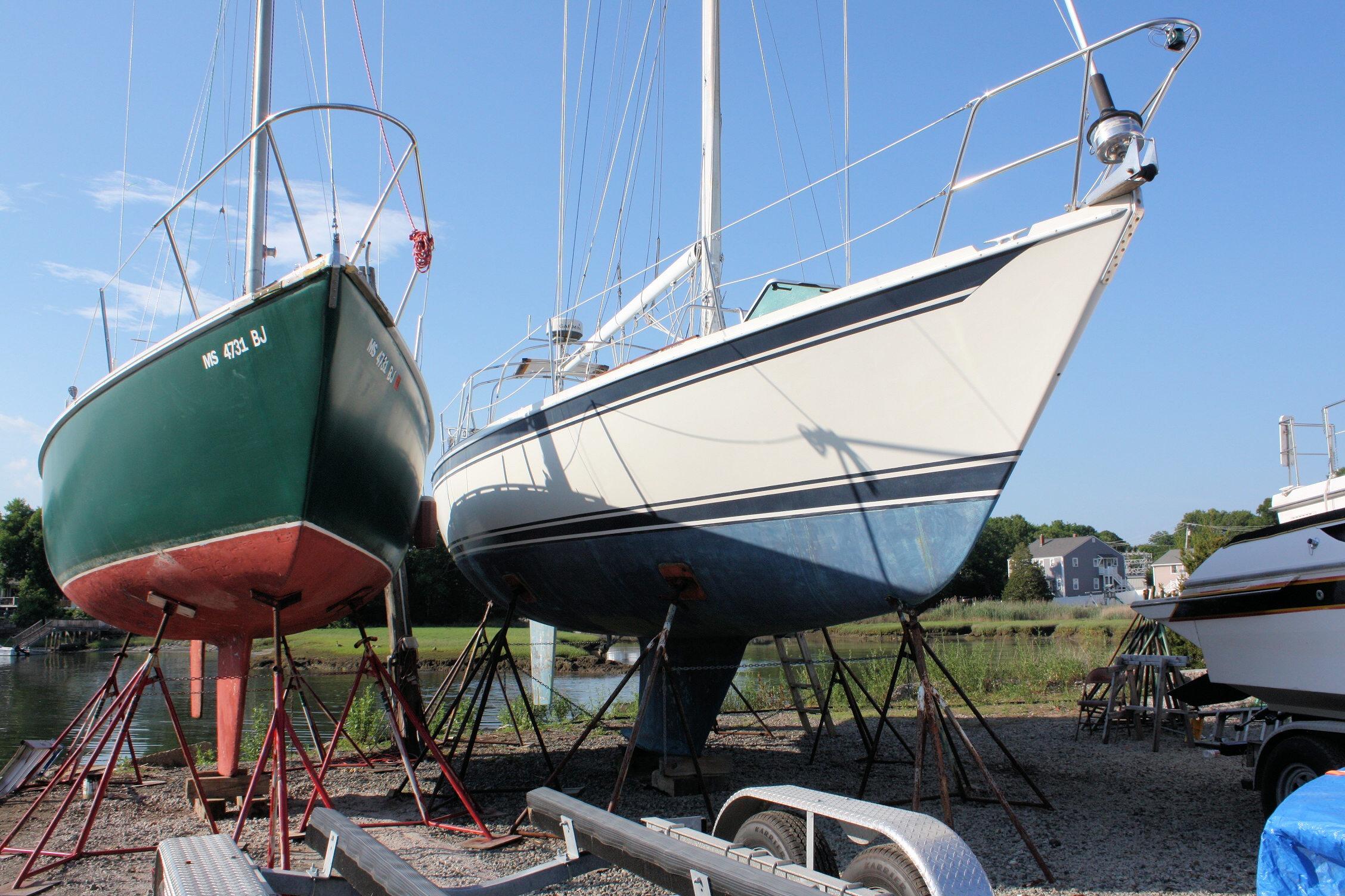 Two sailboats on stands, including a 1987 Ericson 38-200, in a boatyard setting.