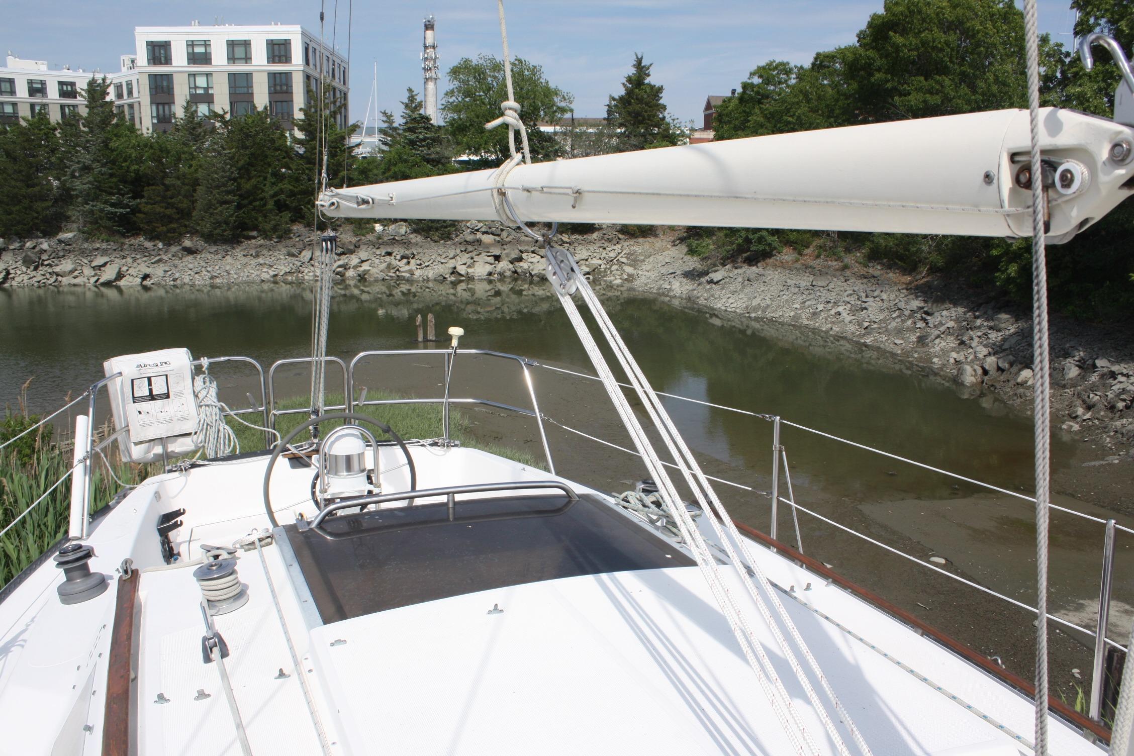 S2 9.2A sailboat from 1981 docked near a rocky shoreline with buildings in the background.