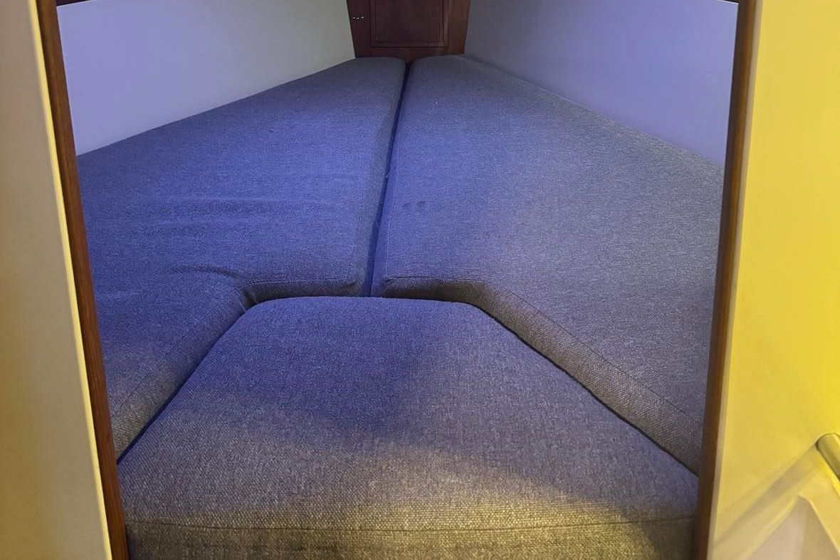 Interior of a boat with blue cushions on a V-shaped sleeping area.