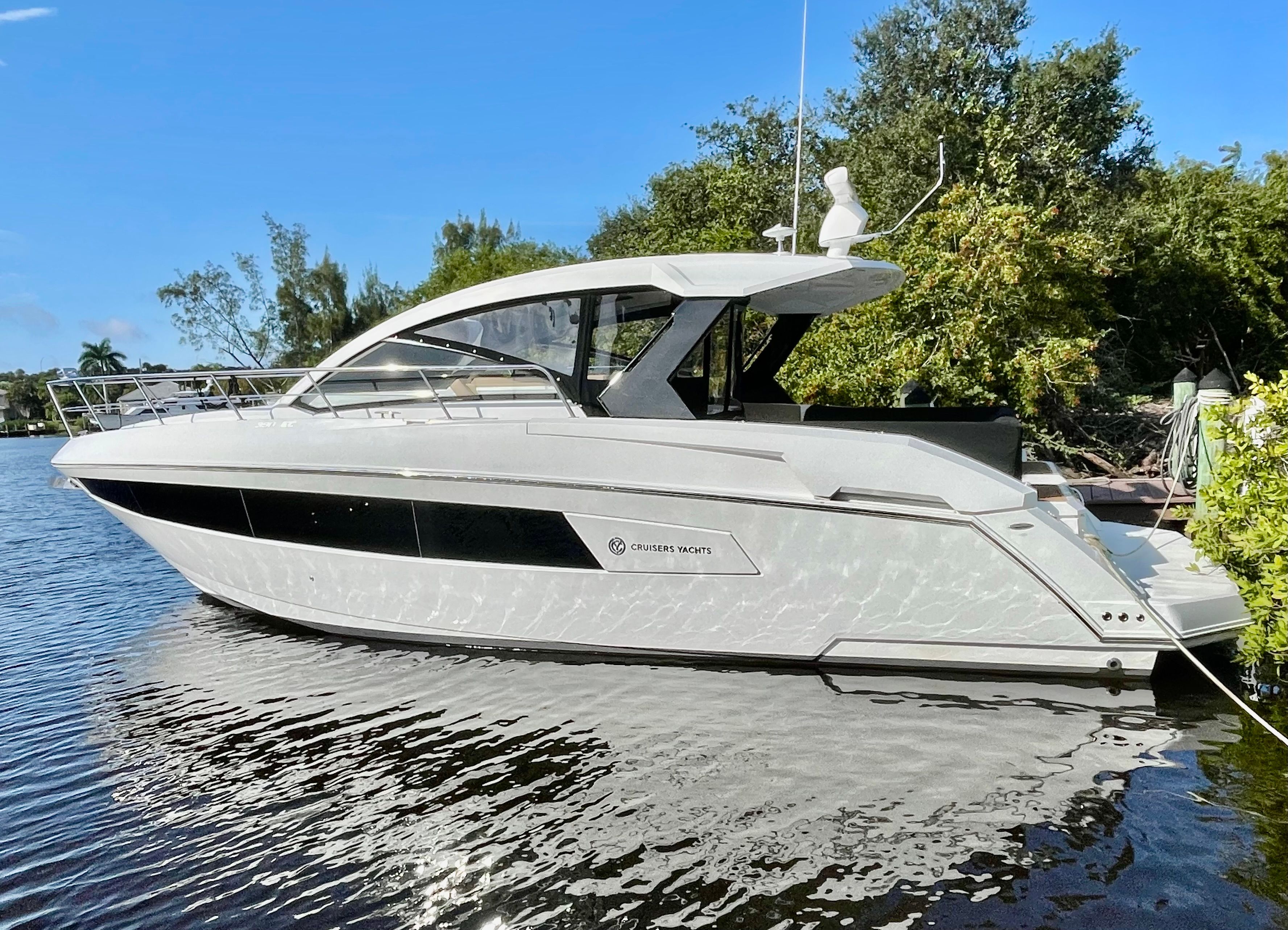 A 2016 Cruisers Yachts 390 Express Coupe sits calmly on the water, surrounded by trees.