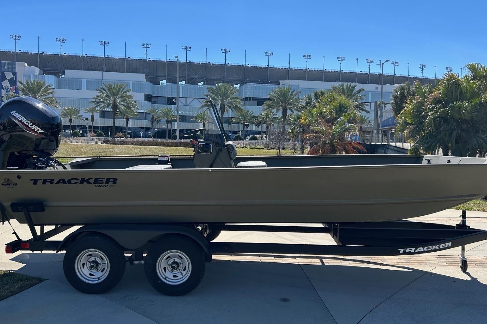 2026 Tracker Grizzly 2072 CC boat on trailer, parked near stadium and palm trees.