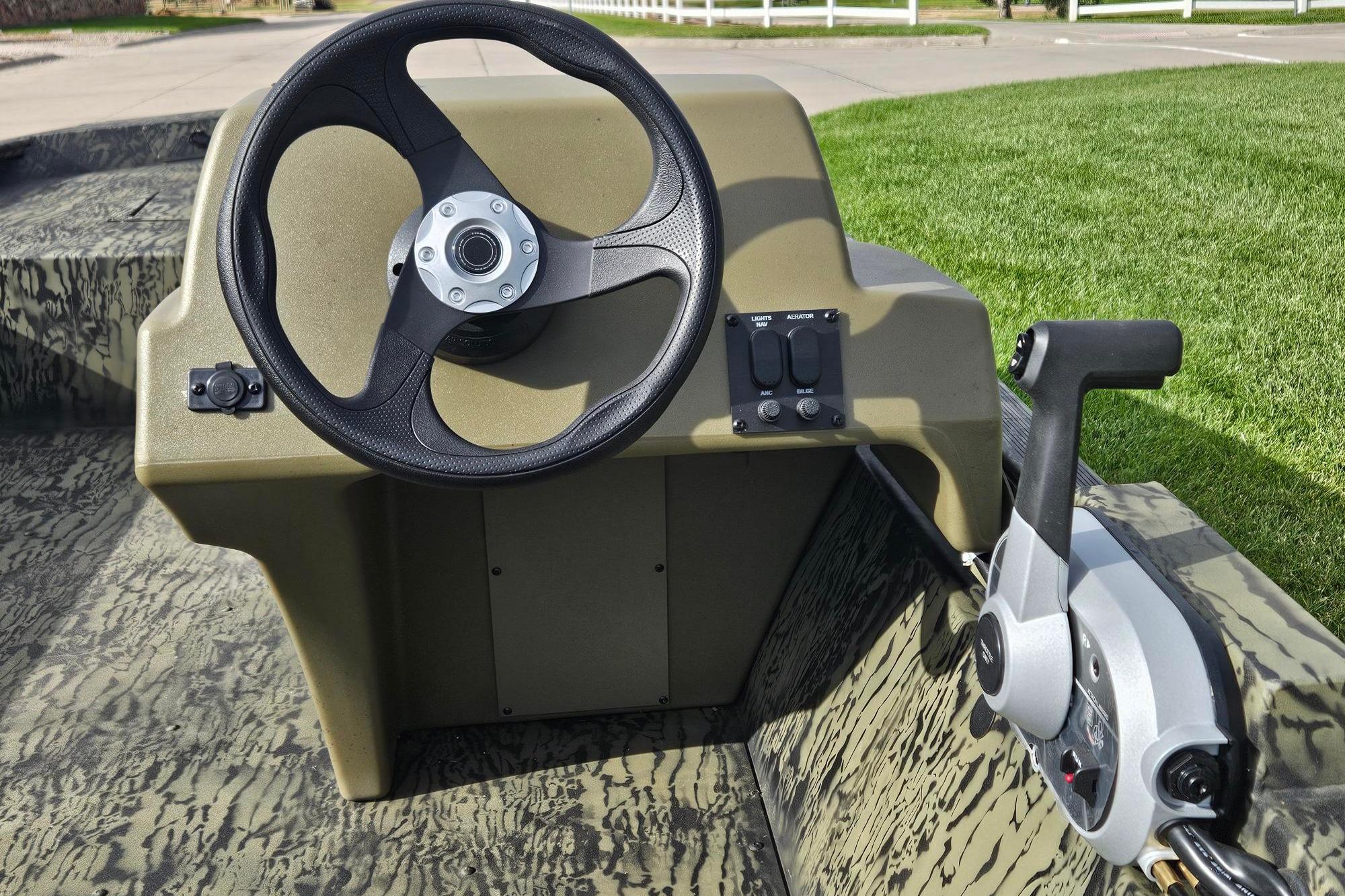 2026 Tracker Grizzly 1648 SC boat steering console with controls, set on a grassy background.