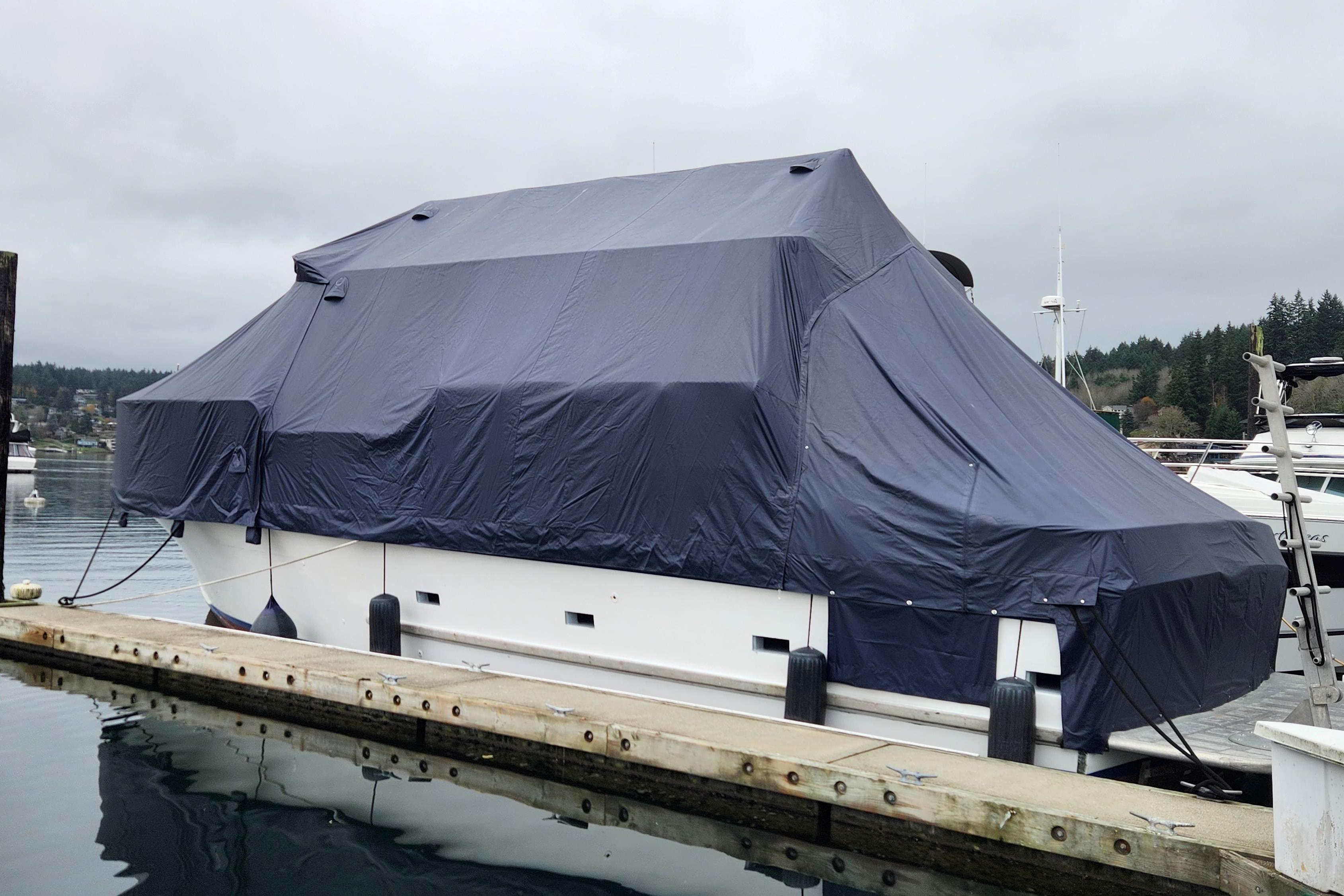 1964 Grandy Tour Boat covered with tarp, docked at marina on a cloudy day.