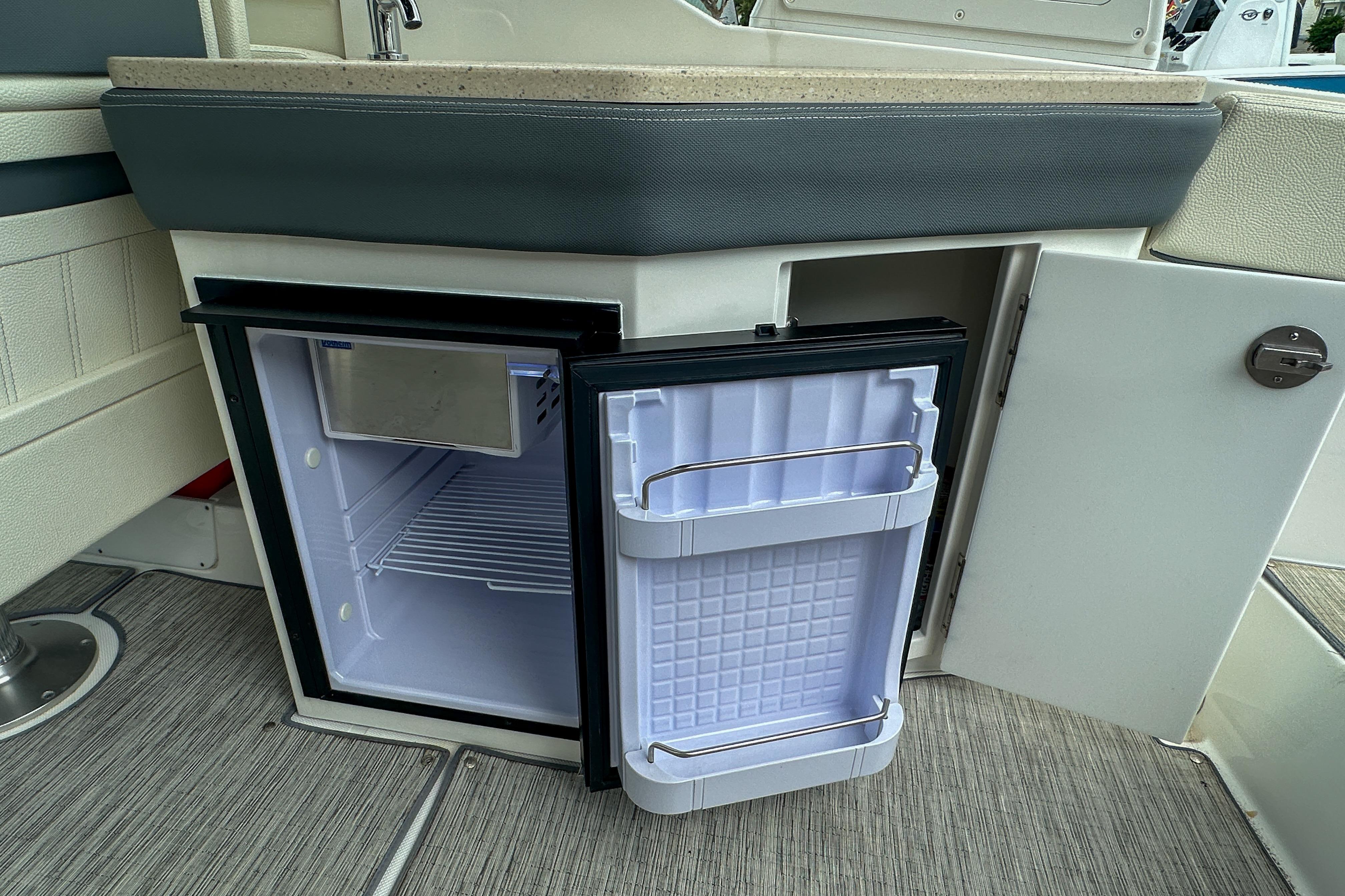 Open mini fridge on 2022 Cobalt 25SC boat, featuring a compact design and storage shelves.