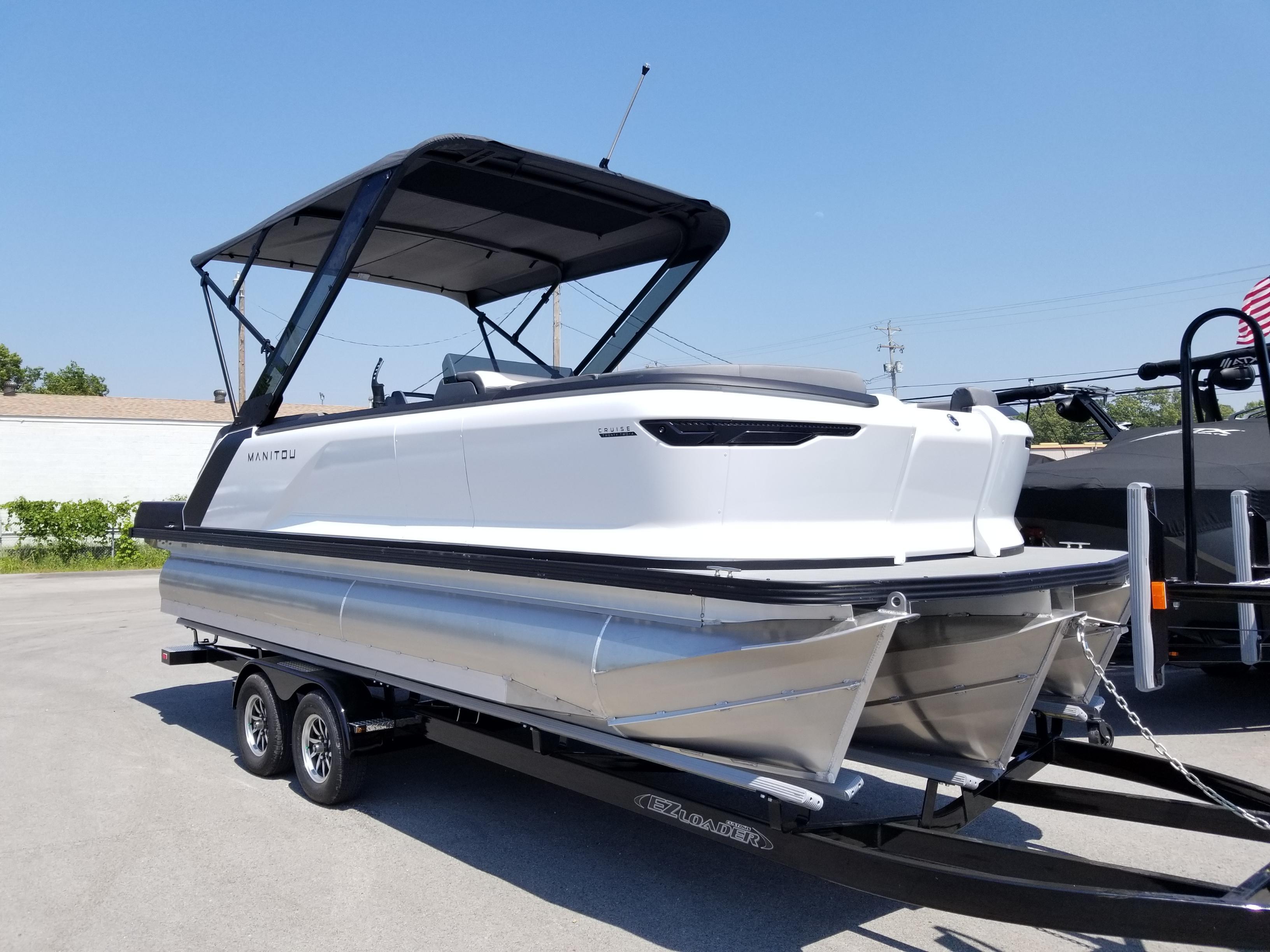 2025 Manitou Cruise pontoon boat on a trailer under clear blue sky.