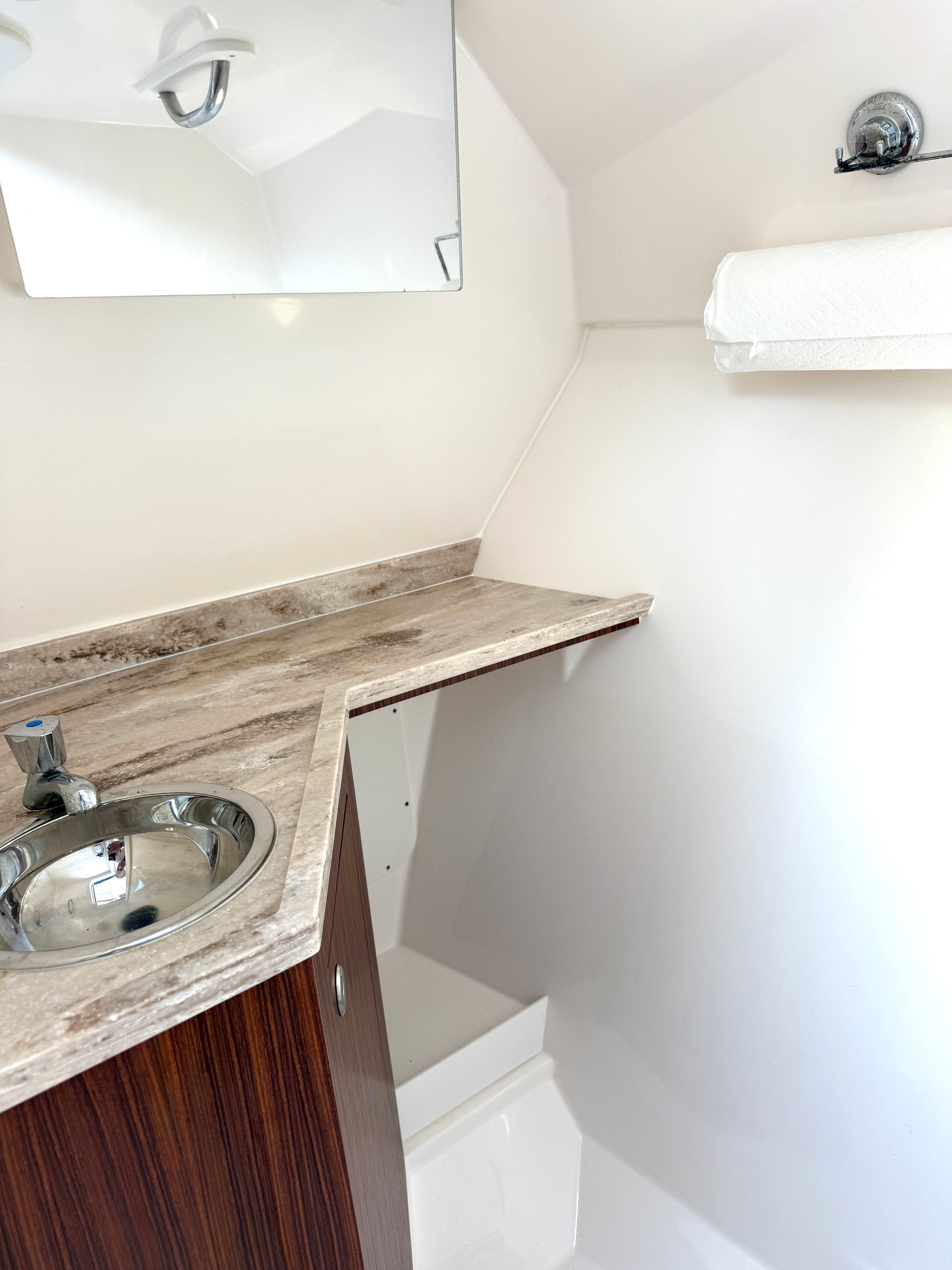Interior view of a boat's washroom with a sink, mirror, and towel holder.