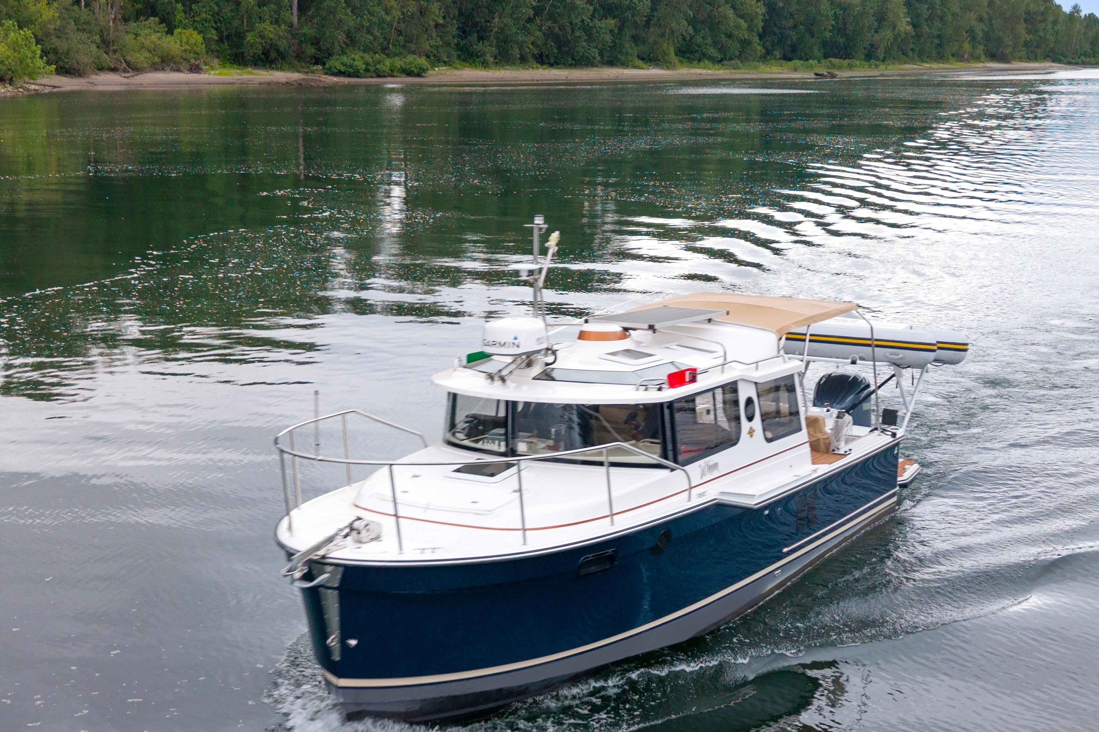 2022 Ranger Tugs R-27 cruising on a serene river with lush green surroundings.