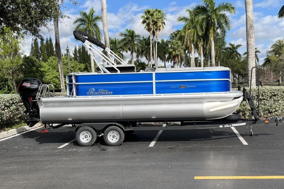 2026 Sun Tracker Party Barge 20 DLX on trailer, surrounded by palm trees.