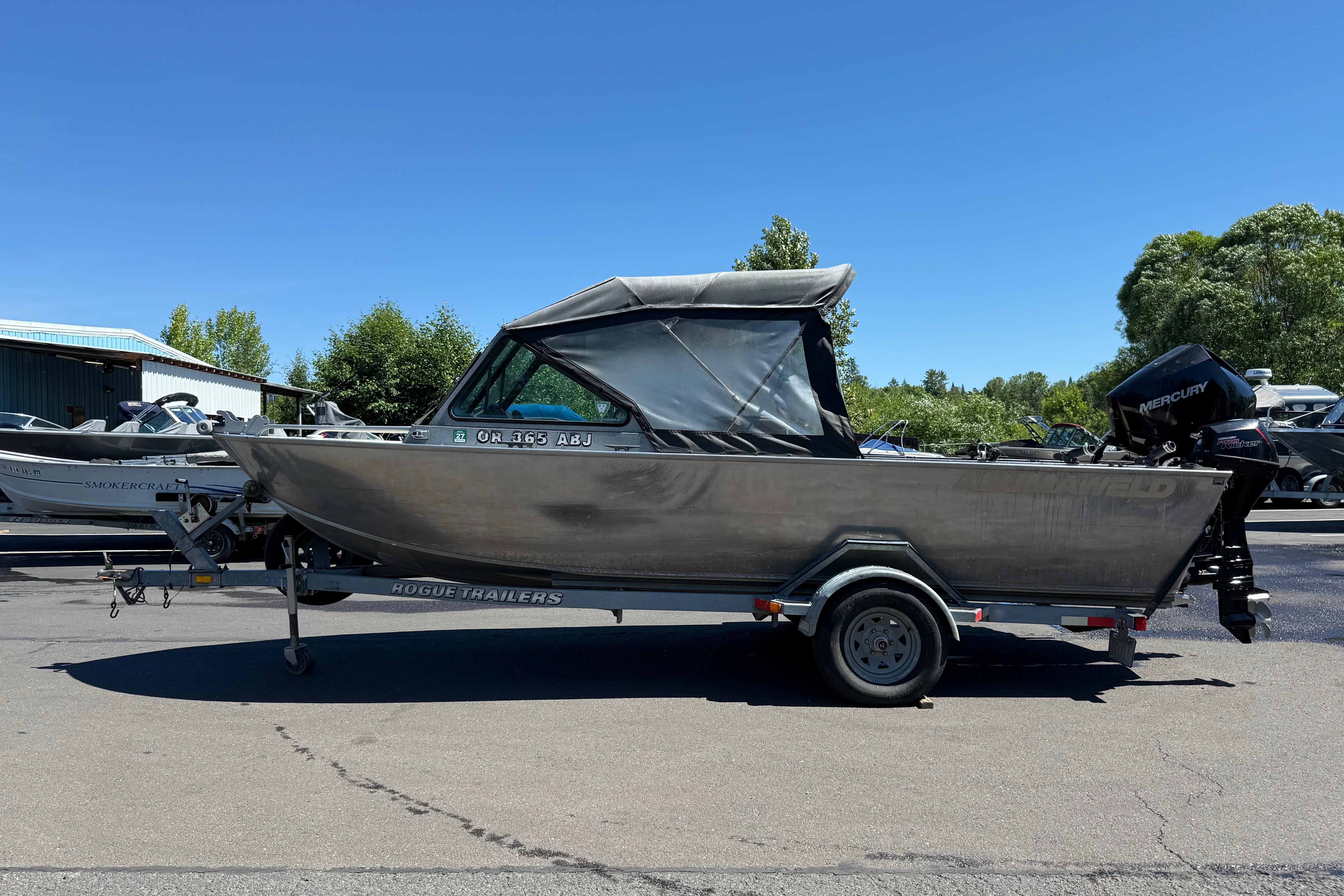 2004 Alumaweld Intruder Outboard 20 boat on trailer, parked outdoors under clear blue sky.