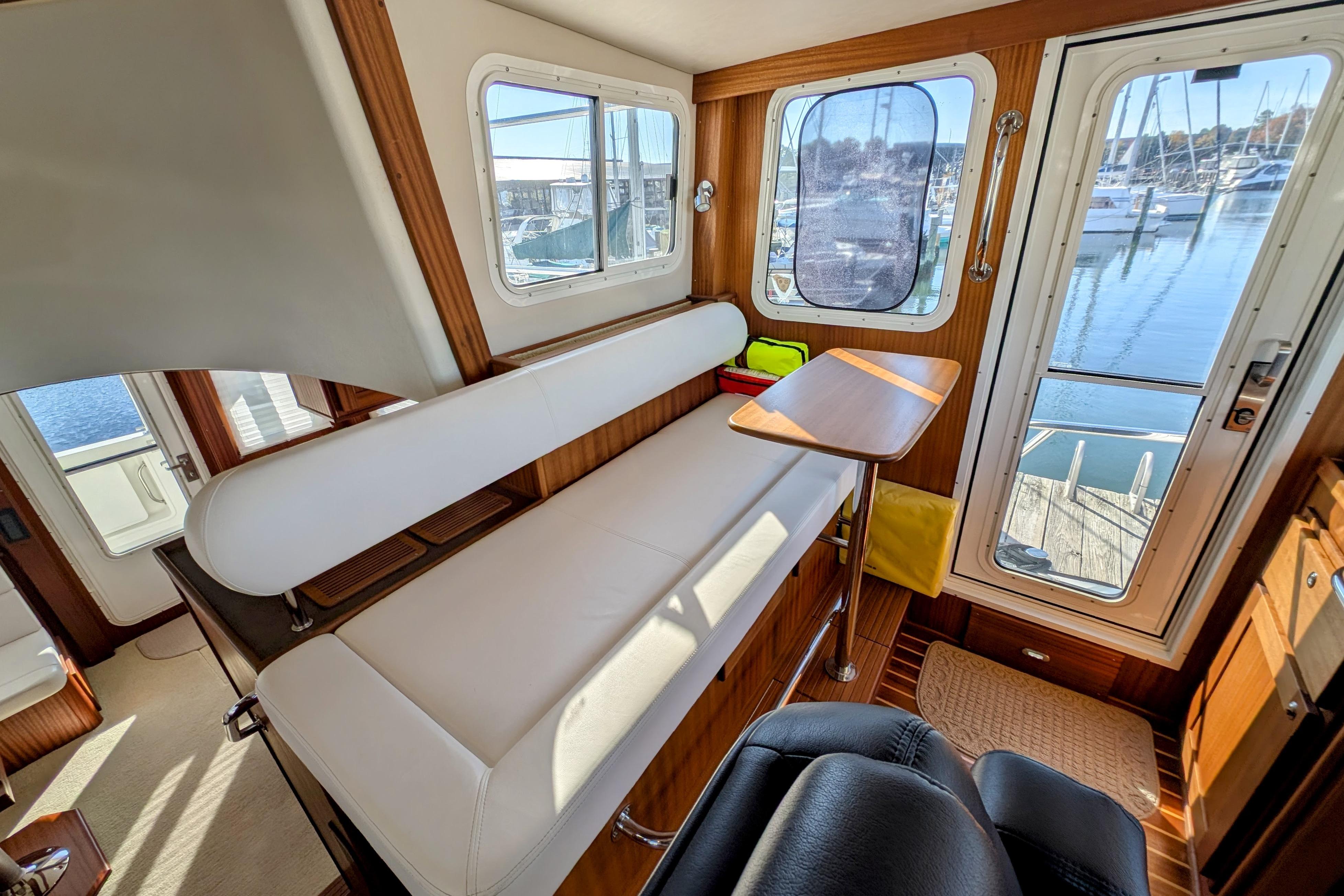 Interior of 2015 American Tug 435 with seating, table, and marina view through windows.