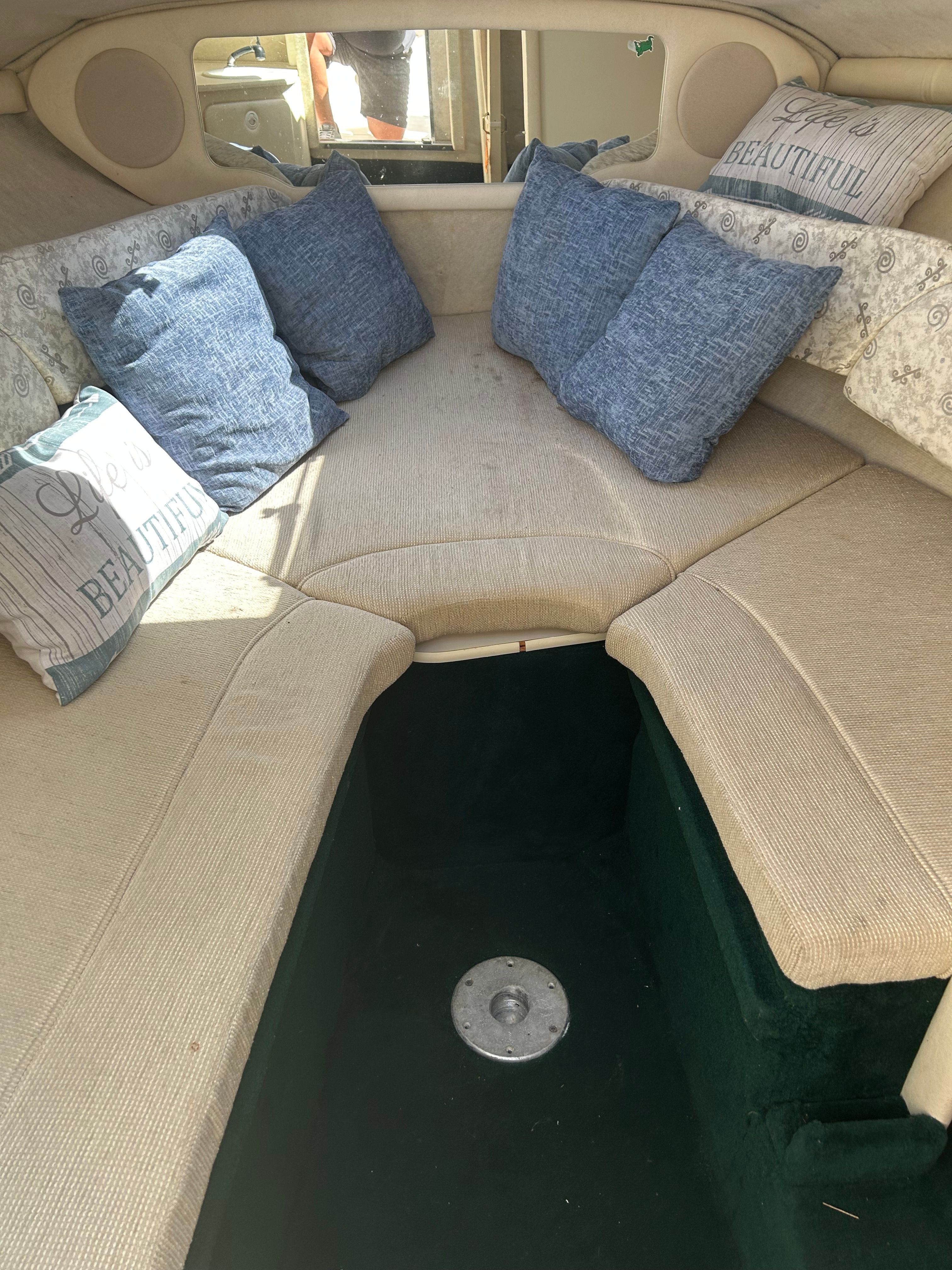 Interior of a 2002 Sea Ray 225 Weekender with beige upholstery and blue cushions.