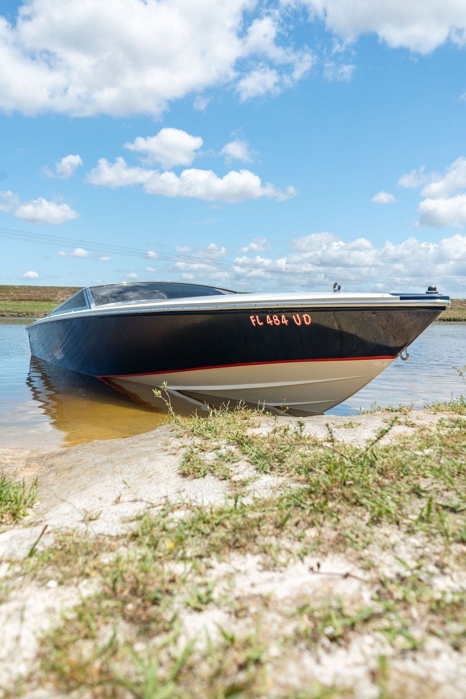 A 1995 Donzi 22 Classic boat is beached on the shore of a body of water.