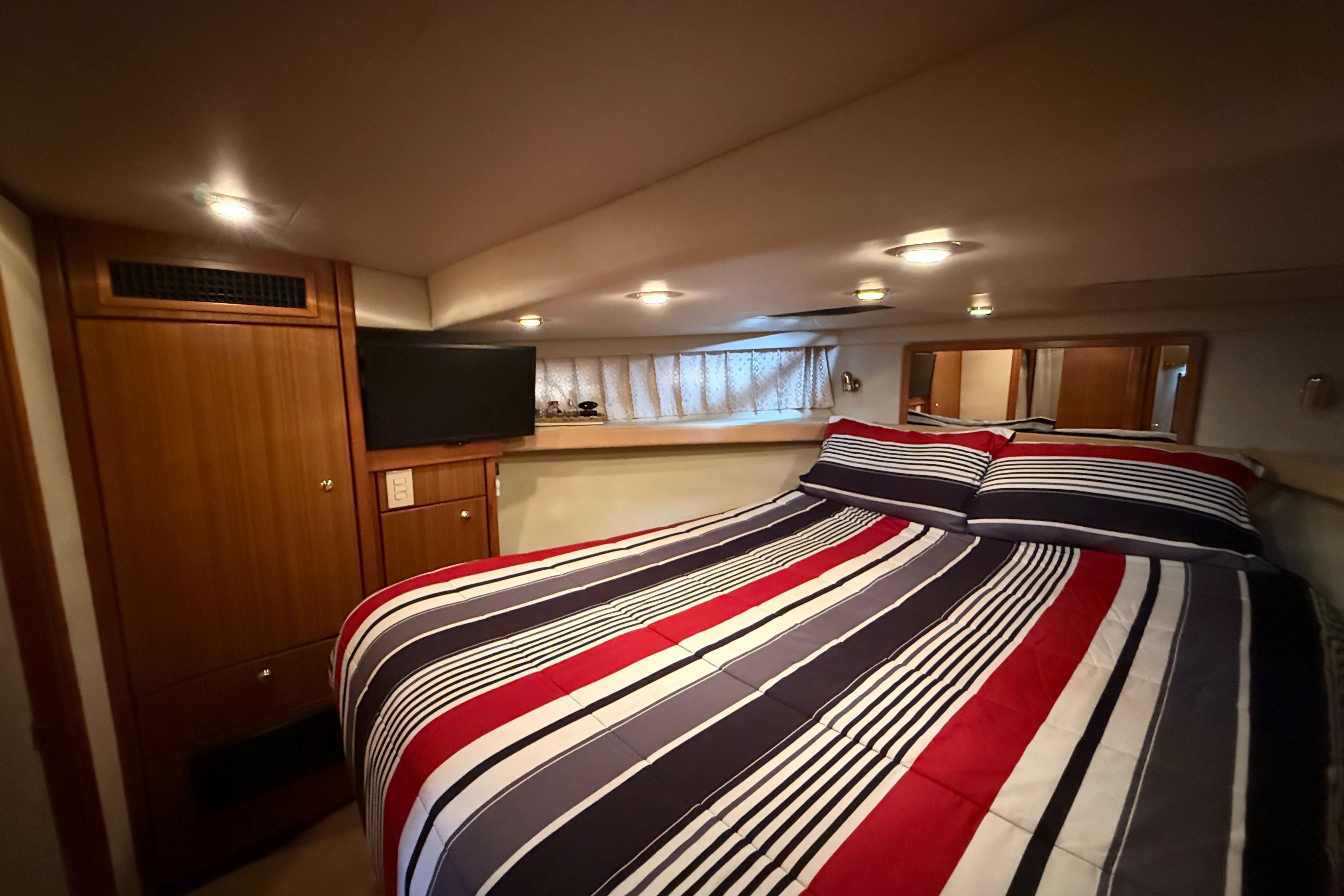 Cozy bedroom in 2002 Bayliner 4788 Pilot House Motoryacht with striped bedding and TV.