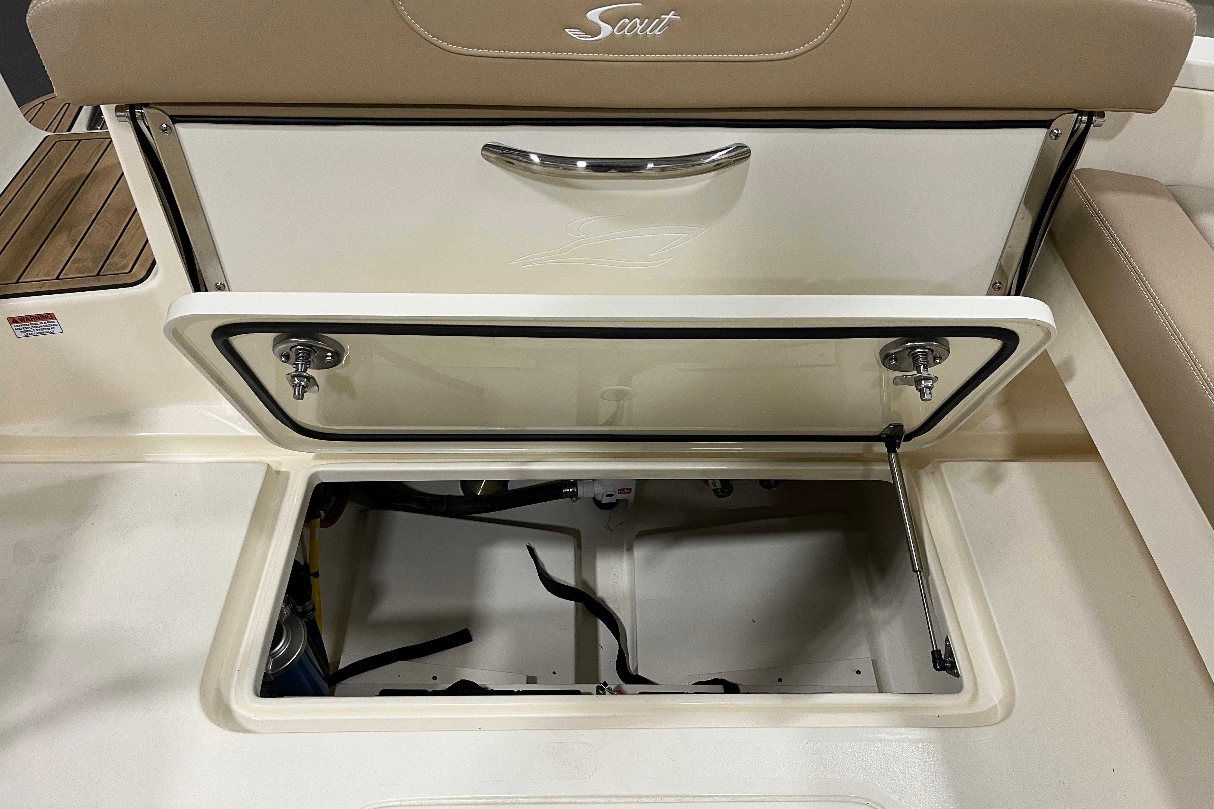 Open storage compartment on 2025 Scout 215 Dorado boat, featuring beige seating and stainless steel handle.