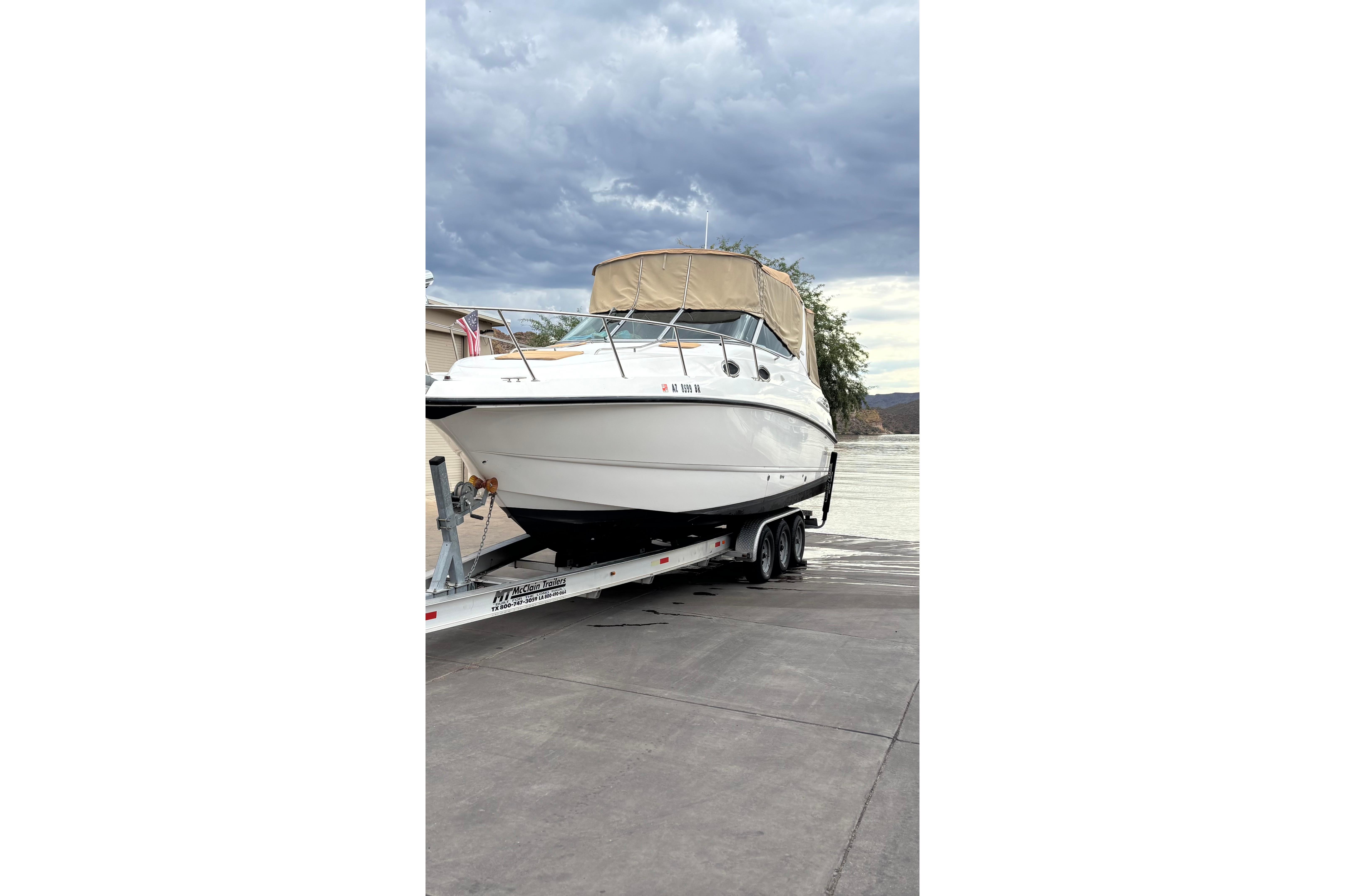 1999 Chaparral Signature 300 boat on trailer by waterfront under cloudy sky.