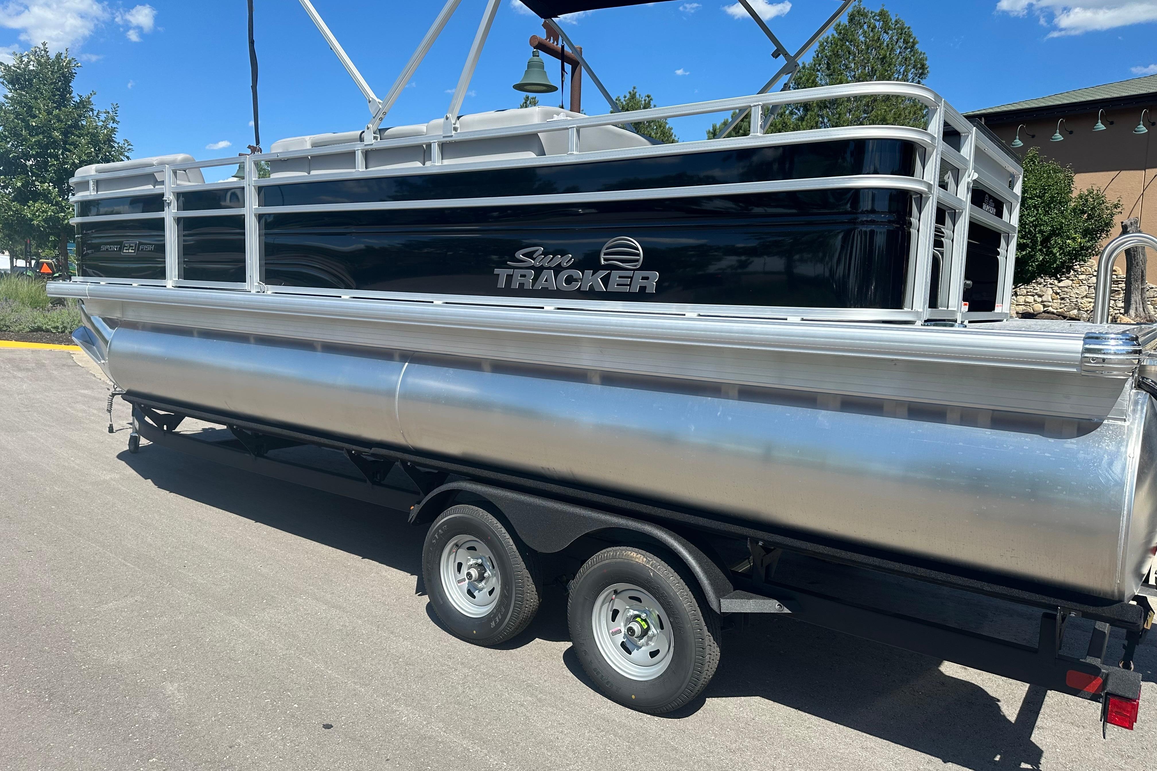 2026 Sun Tracker SportFish 22 DLX pontoon boat on trailer, parked outdoors.