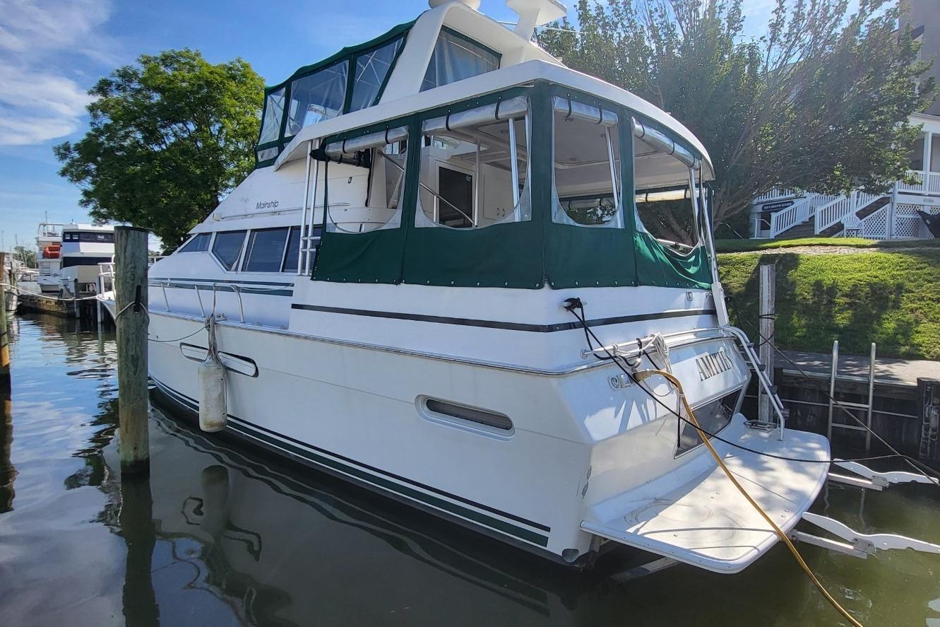 1998 Mainship 47 Motor Yacht docked, featuring green canopy and white hull.