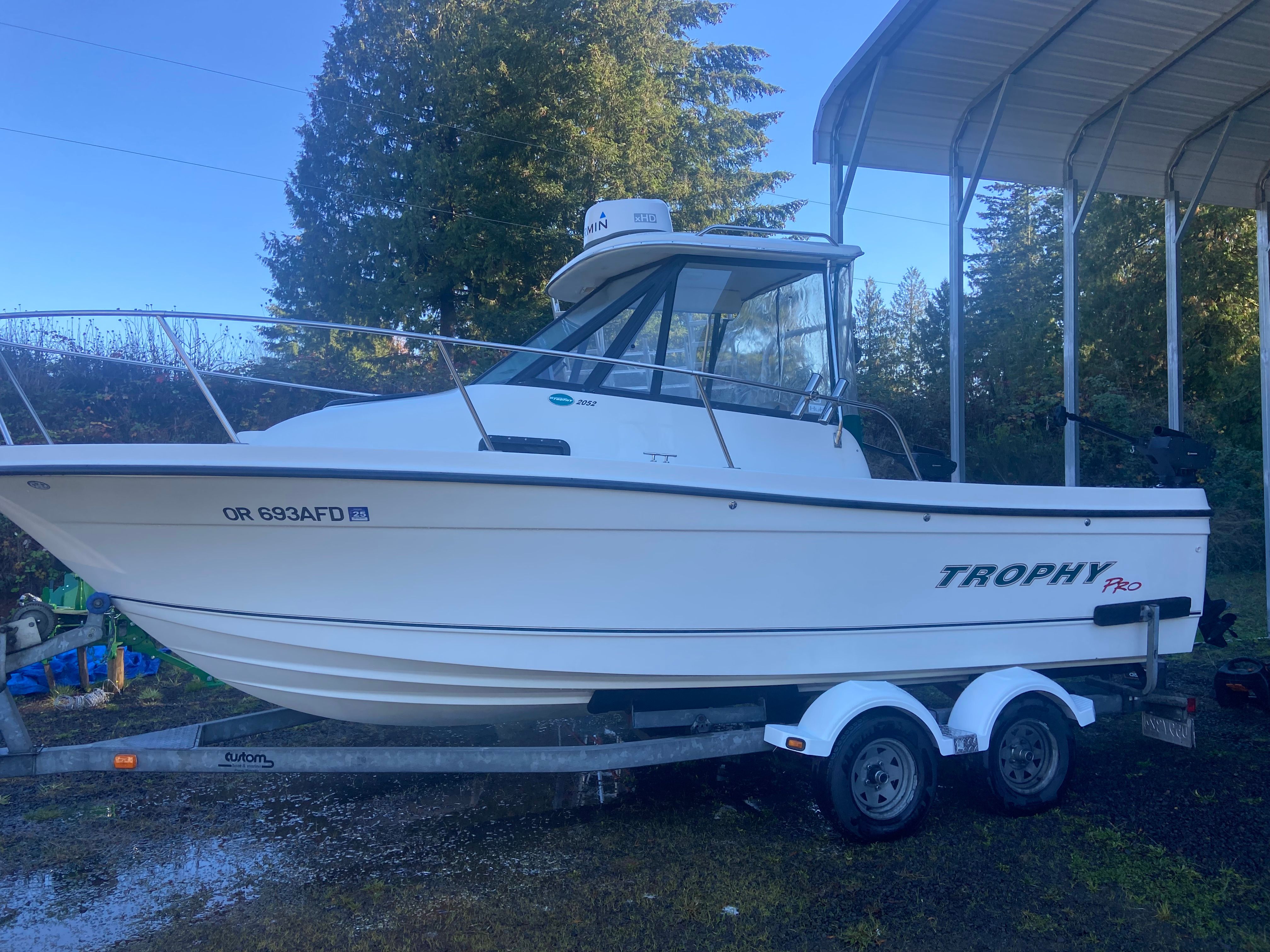 A 2003 Bayliner Trophy Pro 2052 WA boat on a trailer, surrounded by trees.