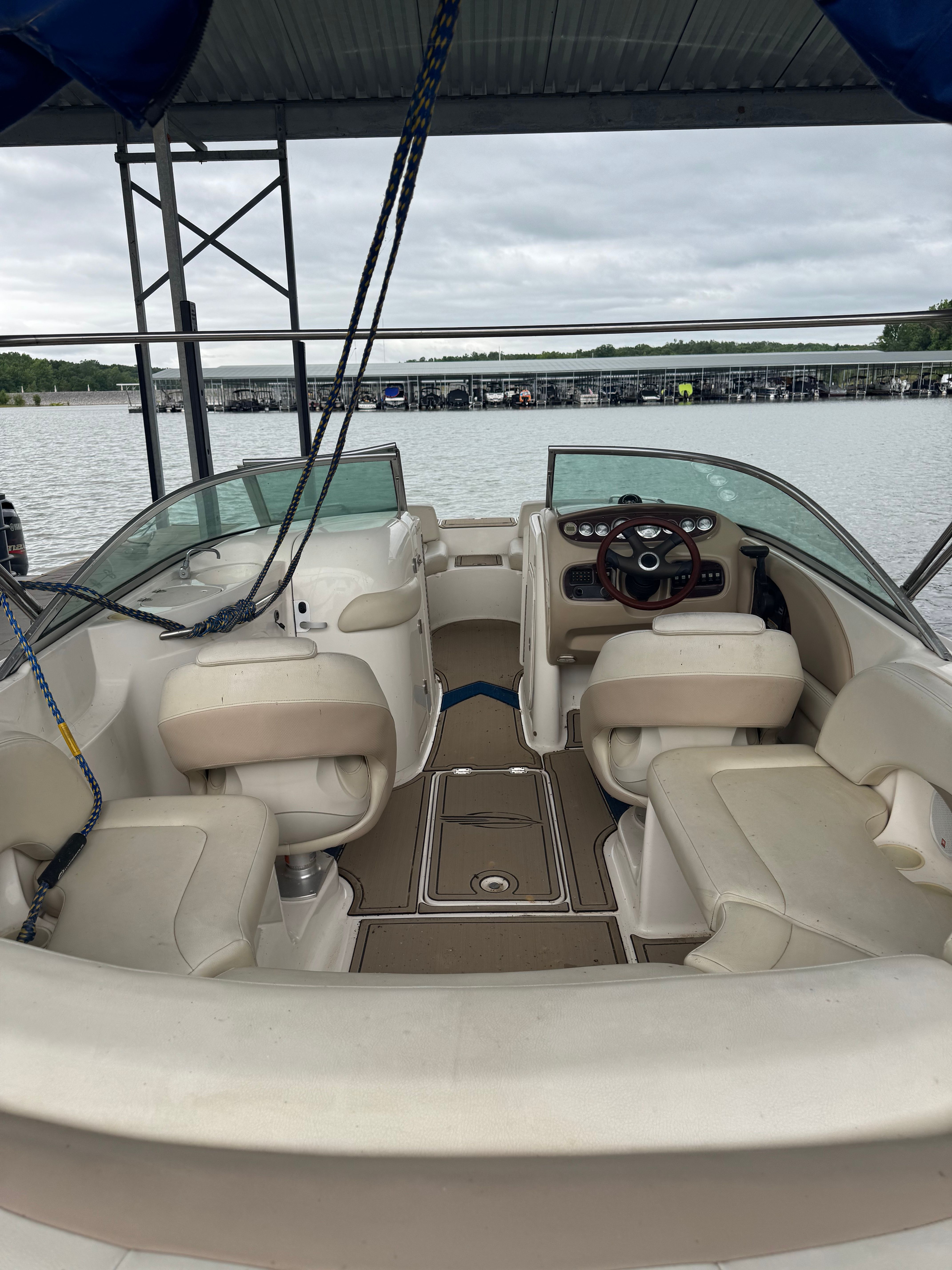 A Chaparral Sunesta 223 boat with beige seats and a steering wheel, docked at a pier.
