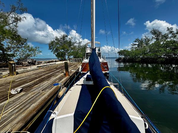 1968 Sailboat 24 docked by a wooden pier, surrounded by lush trees and calm water.