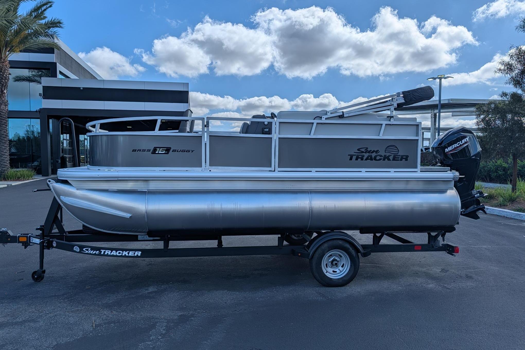 2026 Sun Tracker Bass Buggy 16 XL Select pontoon boat on trailer, parked outdoors.