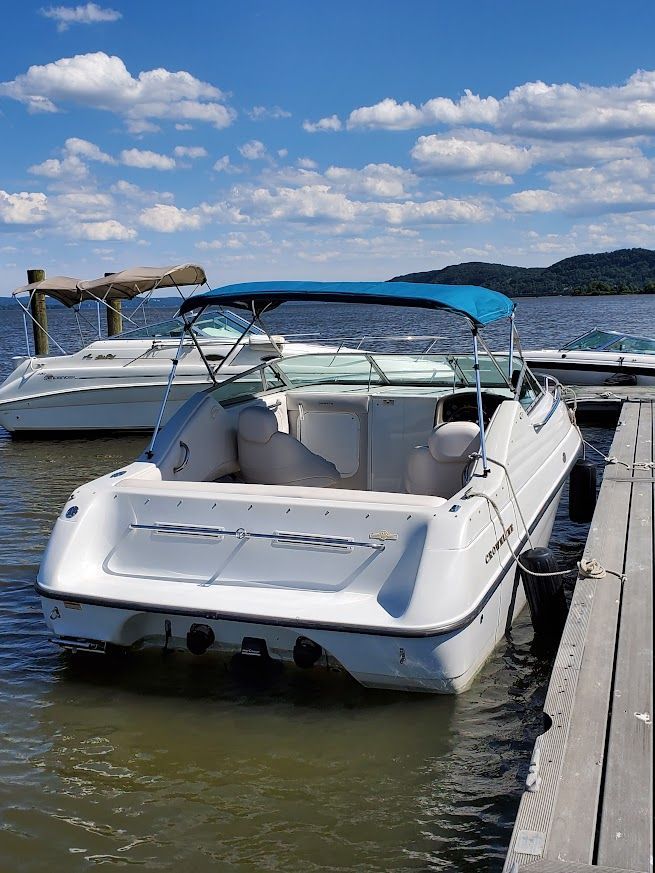 A white boat docked with a blue sunshade, calm water, and distant hills in the background.
