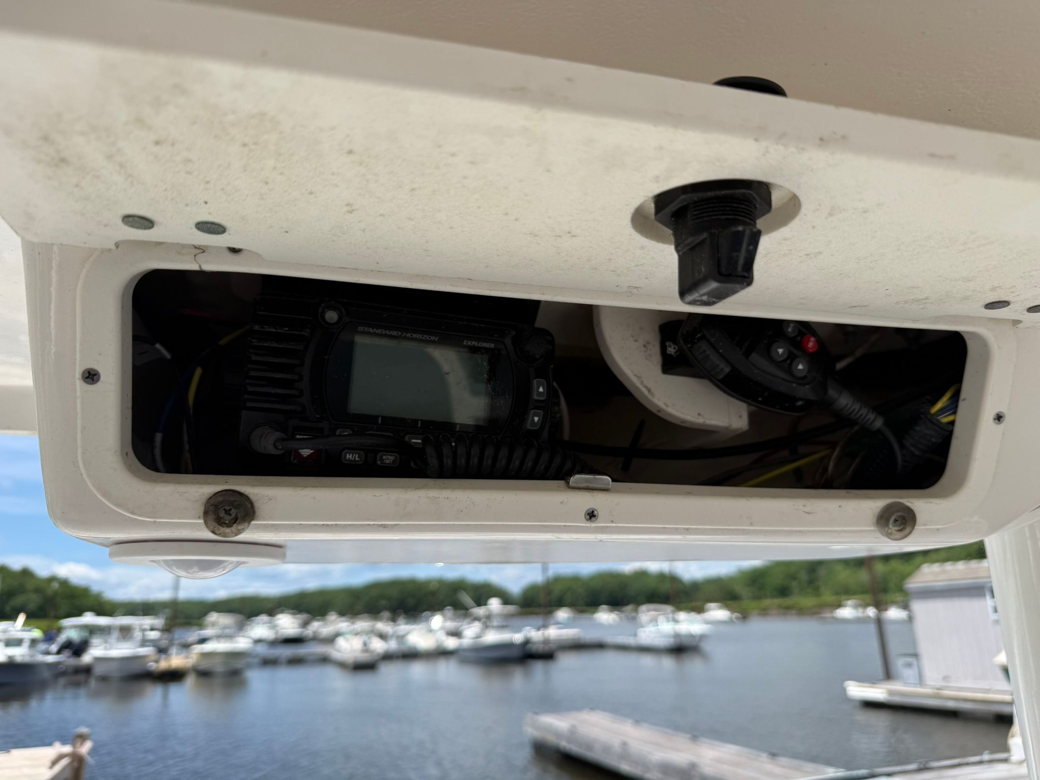 An open compartment with electronic equipment on a boat, with a marina in the background.