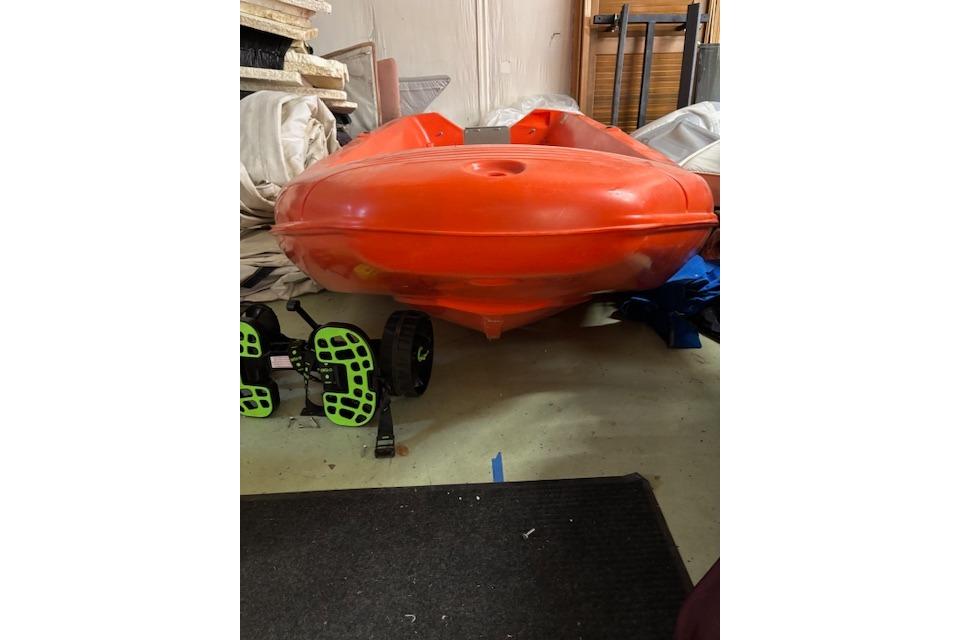 Bright orange River Boats 350 kayak, 2022 model, stored indoors with equipment nearby.