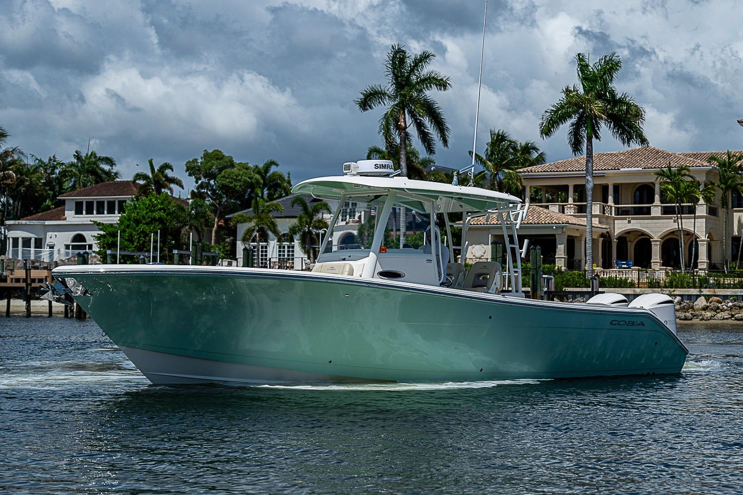 2019 Cobia 320 Center Console boat cruising near luxury waterfront homes.