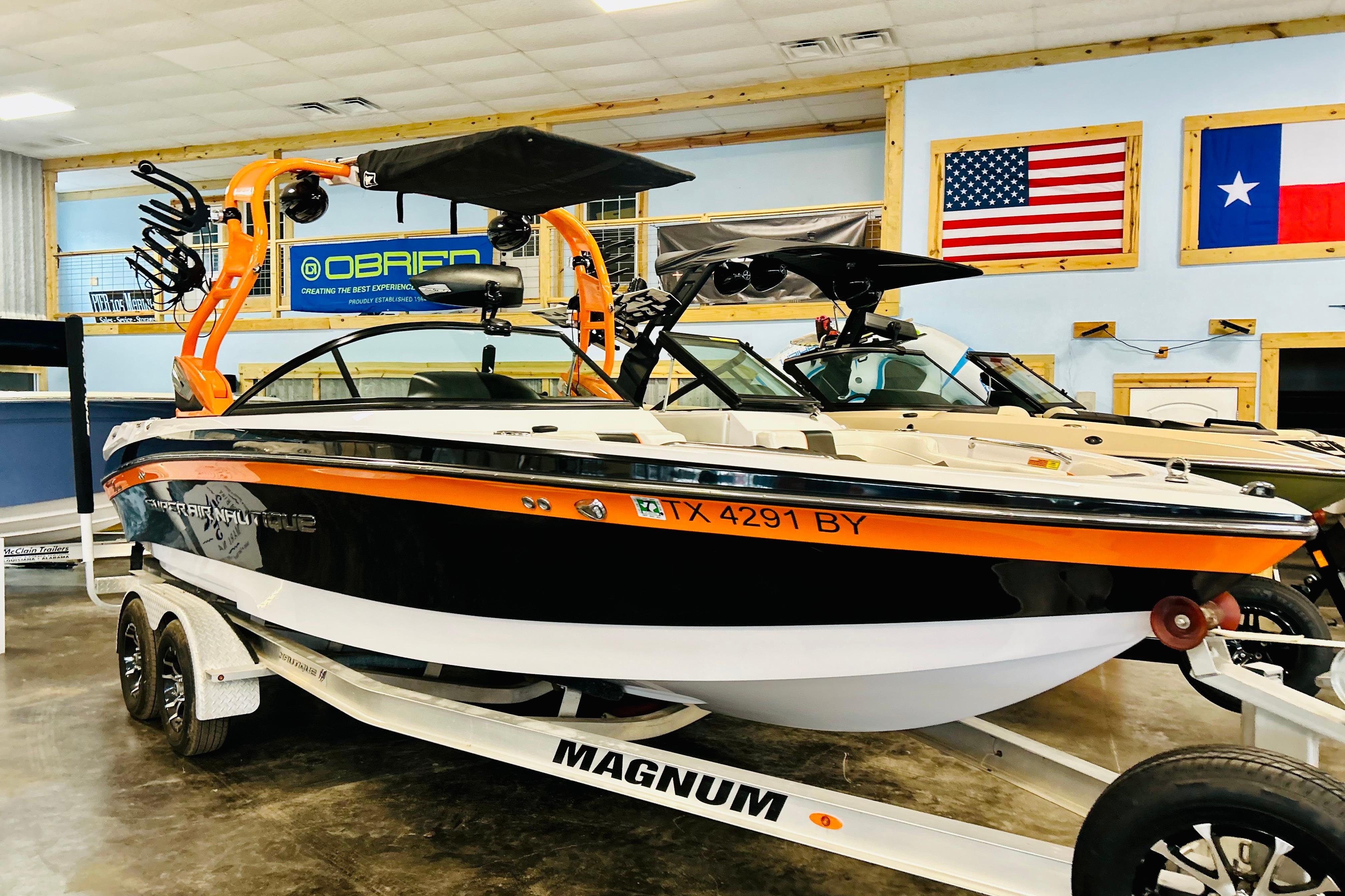 2013 Nautique Super Air Nautique 230 boat on trailer in showroom with flags displayed.