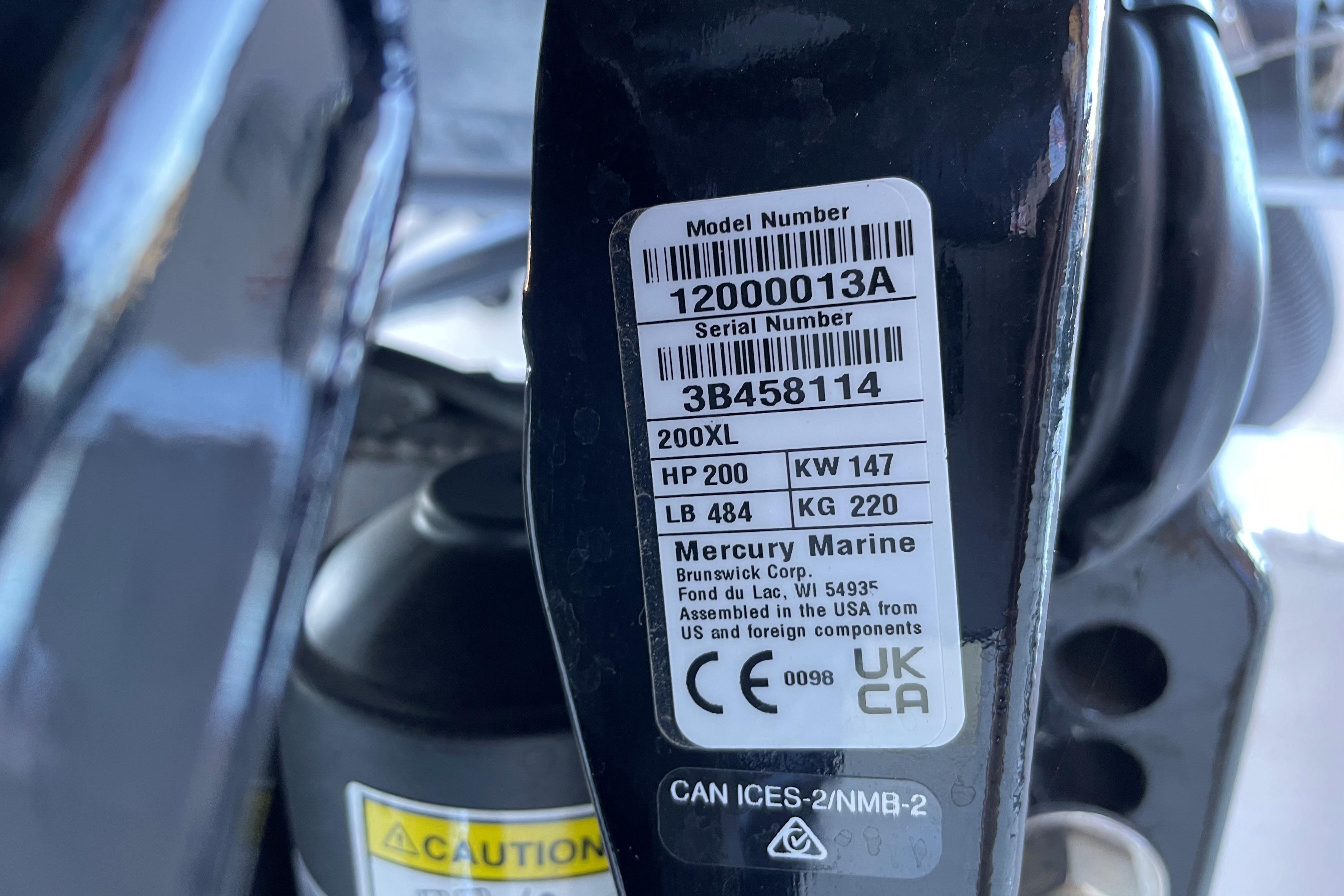 Label on Mercury Marine engine, showing model and serial numbers, with caution sign.