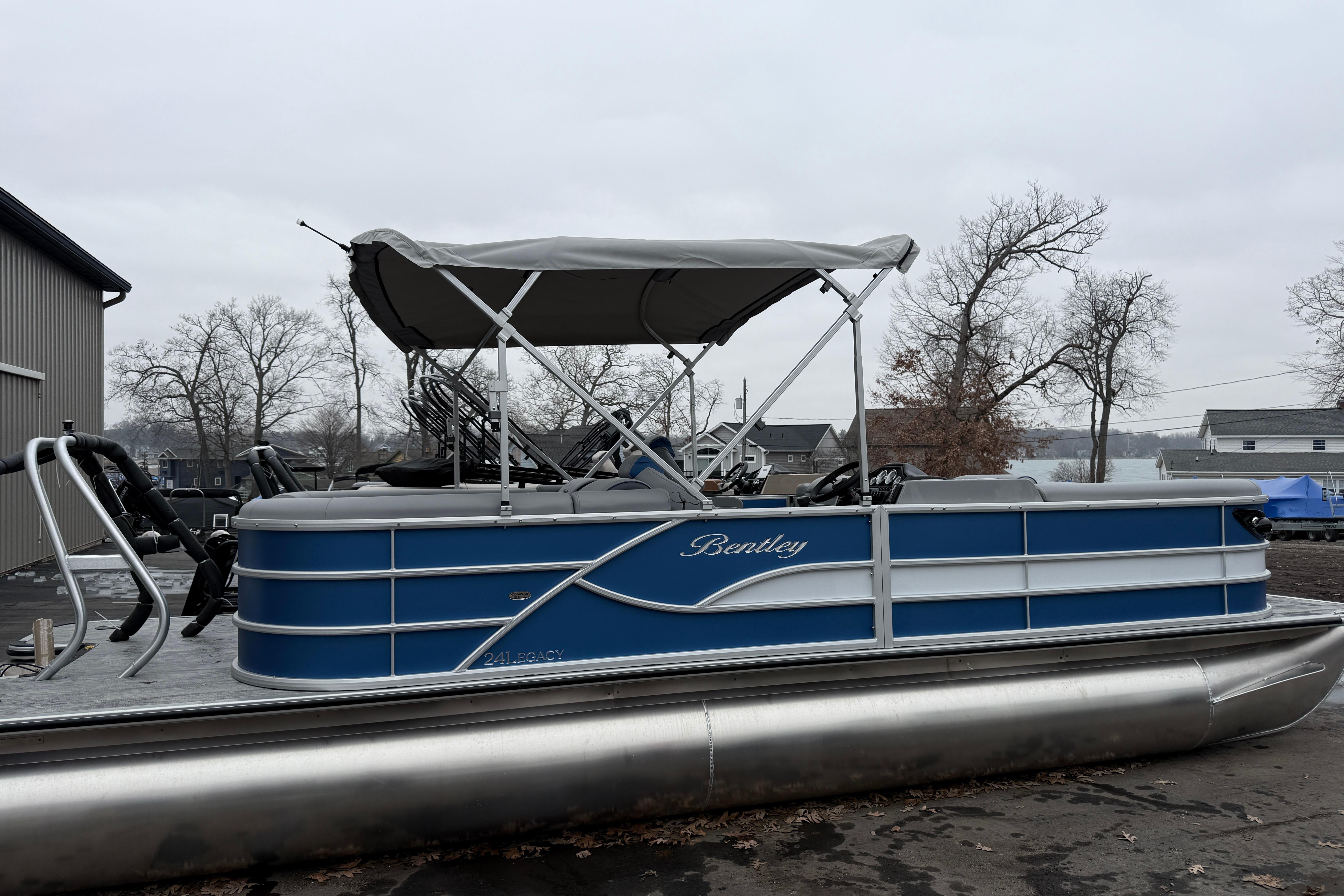 2026 Bentley Pontoons Legacy 240 Navigator Ext, blue pontoon boat with canopy, parked outdoors.