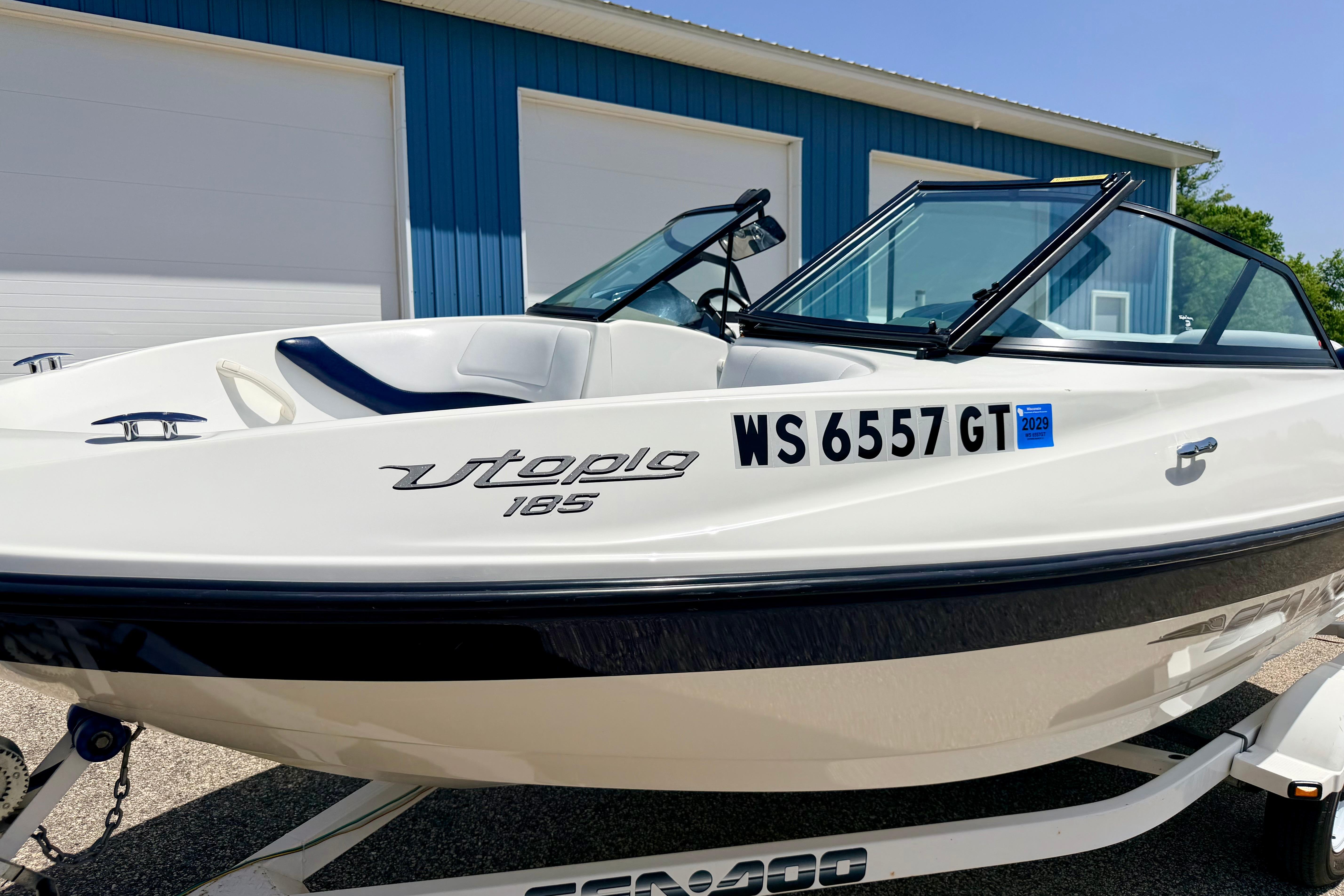 2004 Bombardier SEADOO Utopia 185 boat on trailer, parked near blue building.