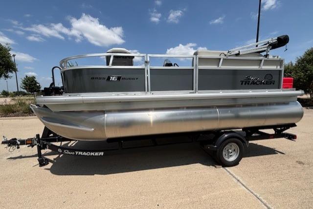 2026 Sun Tracker Bass Buggy 16 XL Select pontoon boat on trailer, parked outdoors.
