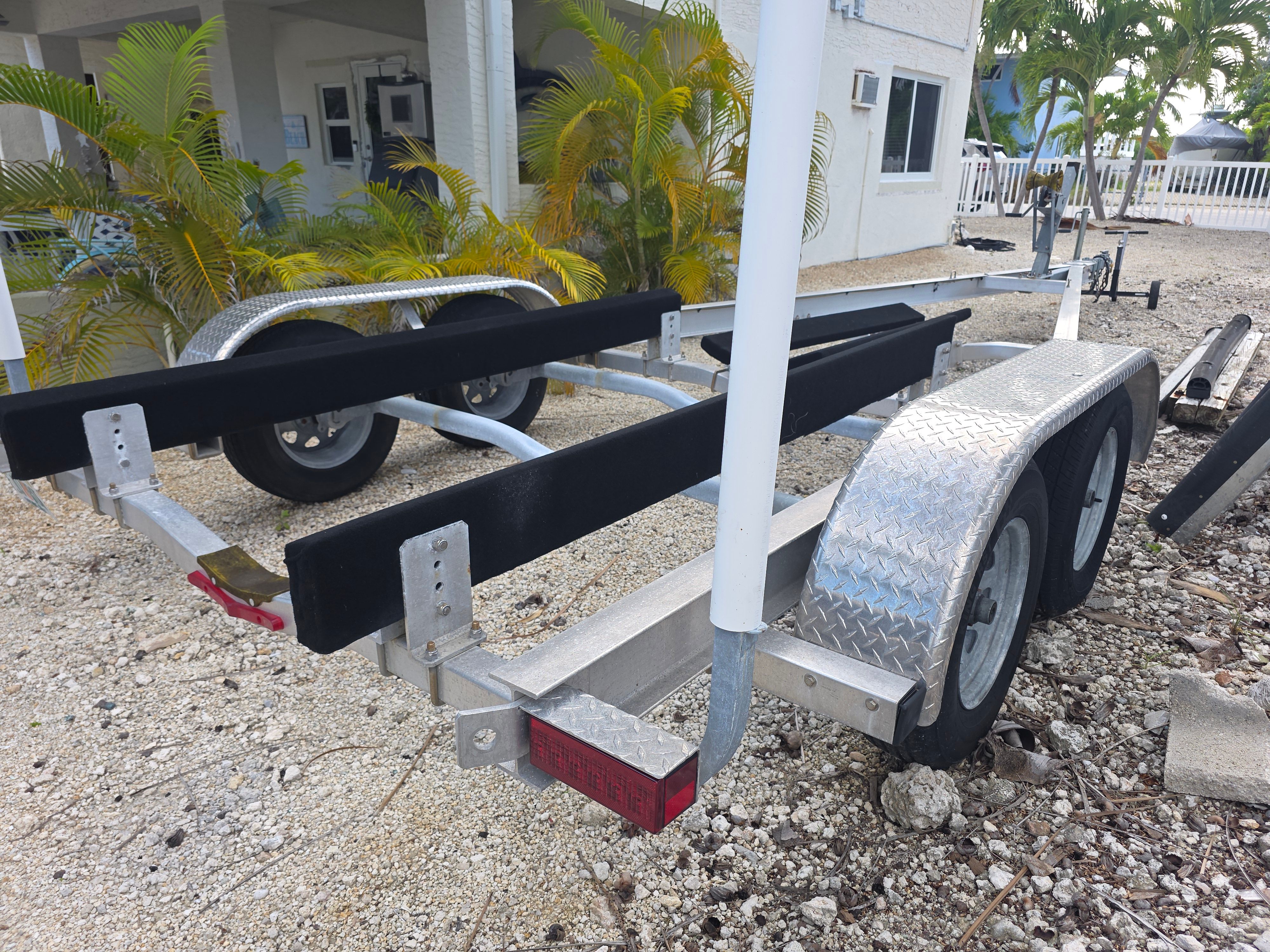 Boat trailer on gravel with plants in background.