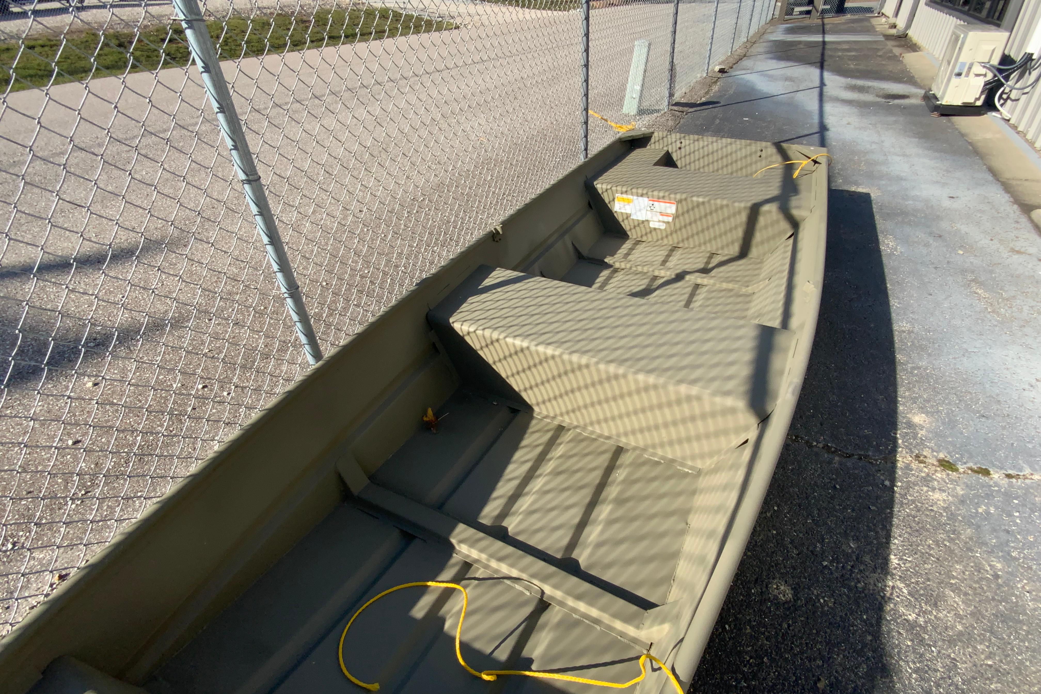 2026 Tracker Grizzly 14 Jon boat parked near chain-link fence.