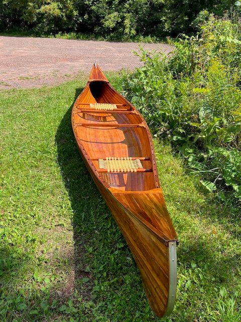 A handcrafted cedar strip canoe sits on a grassy area.