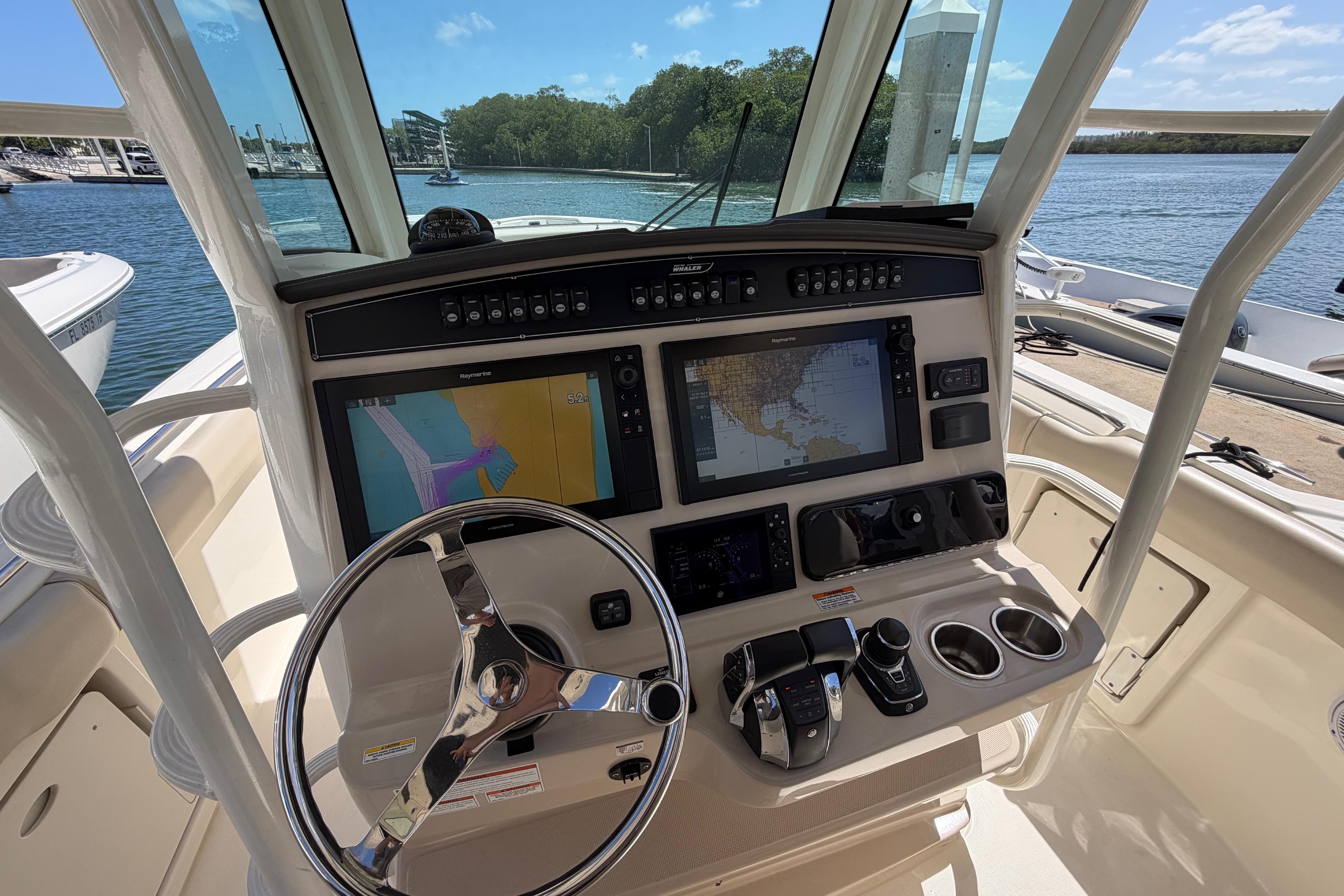 2019 Boston Whaler 330 Outrage helm with navigation screens and controls, docked by the water.