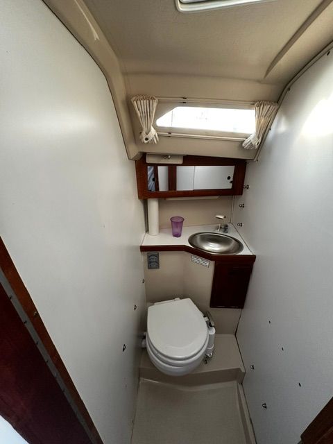 Interior view of a boat bathroom with toilet, sink, and window.