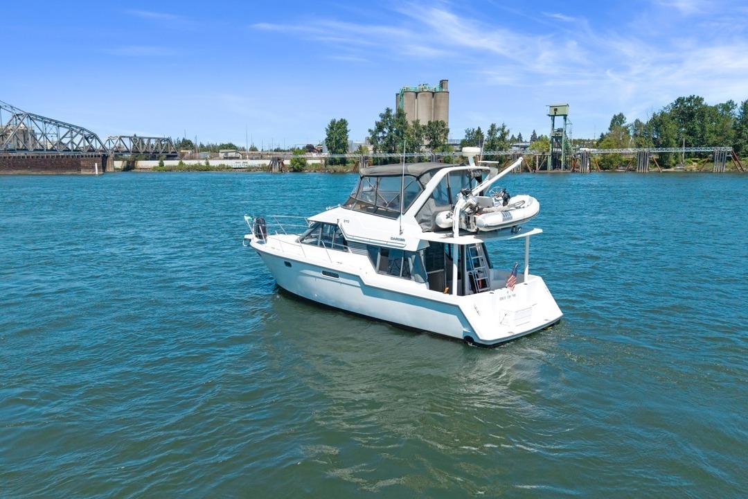 1994 Carver 370 Voyager yacht on a river with industrial backdrop.