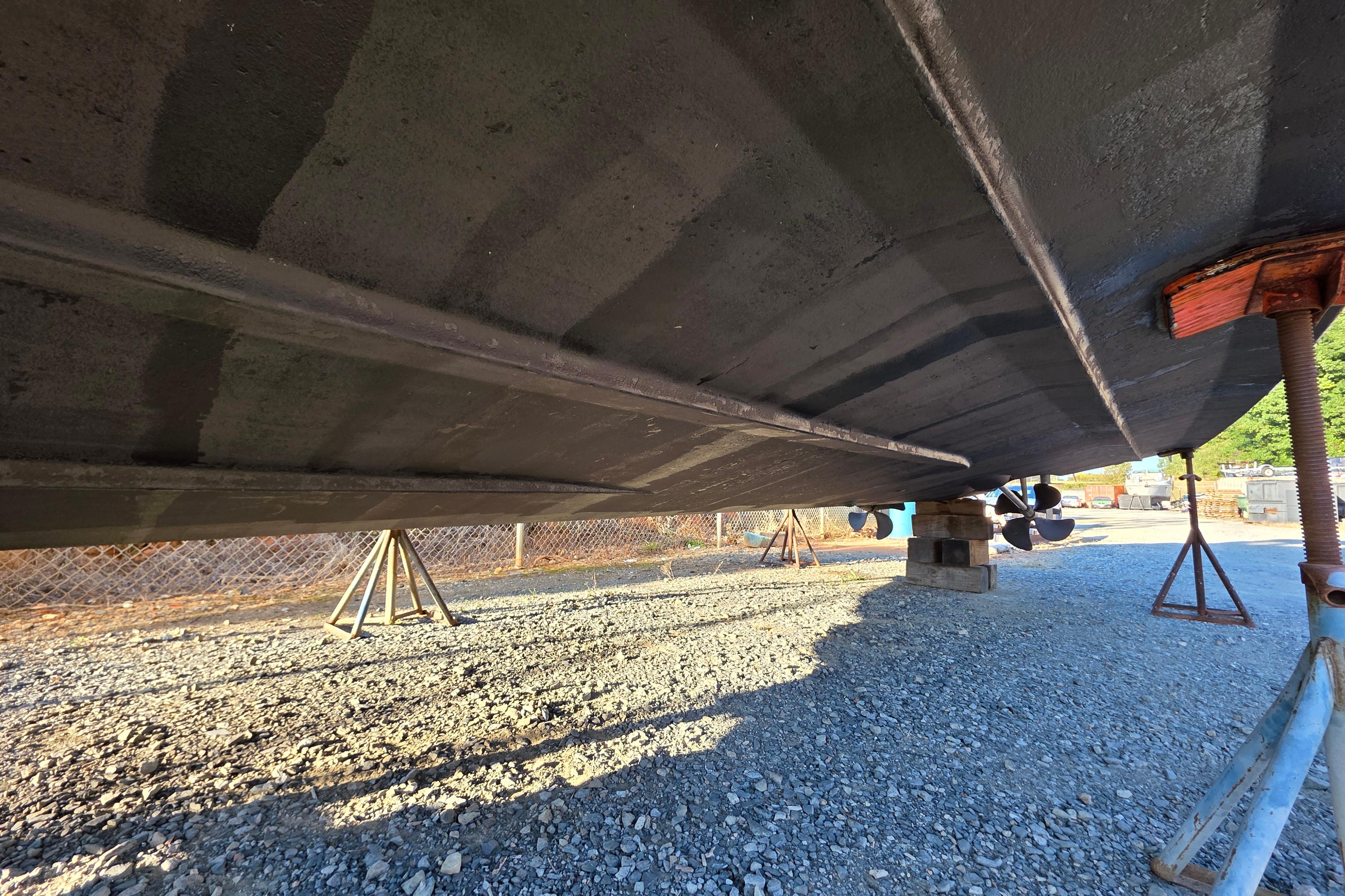 Underside view of 1998 Maxum 3700 SCR boat on stands, gravel ground.