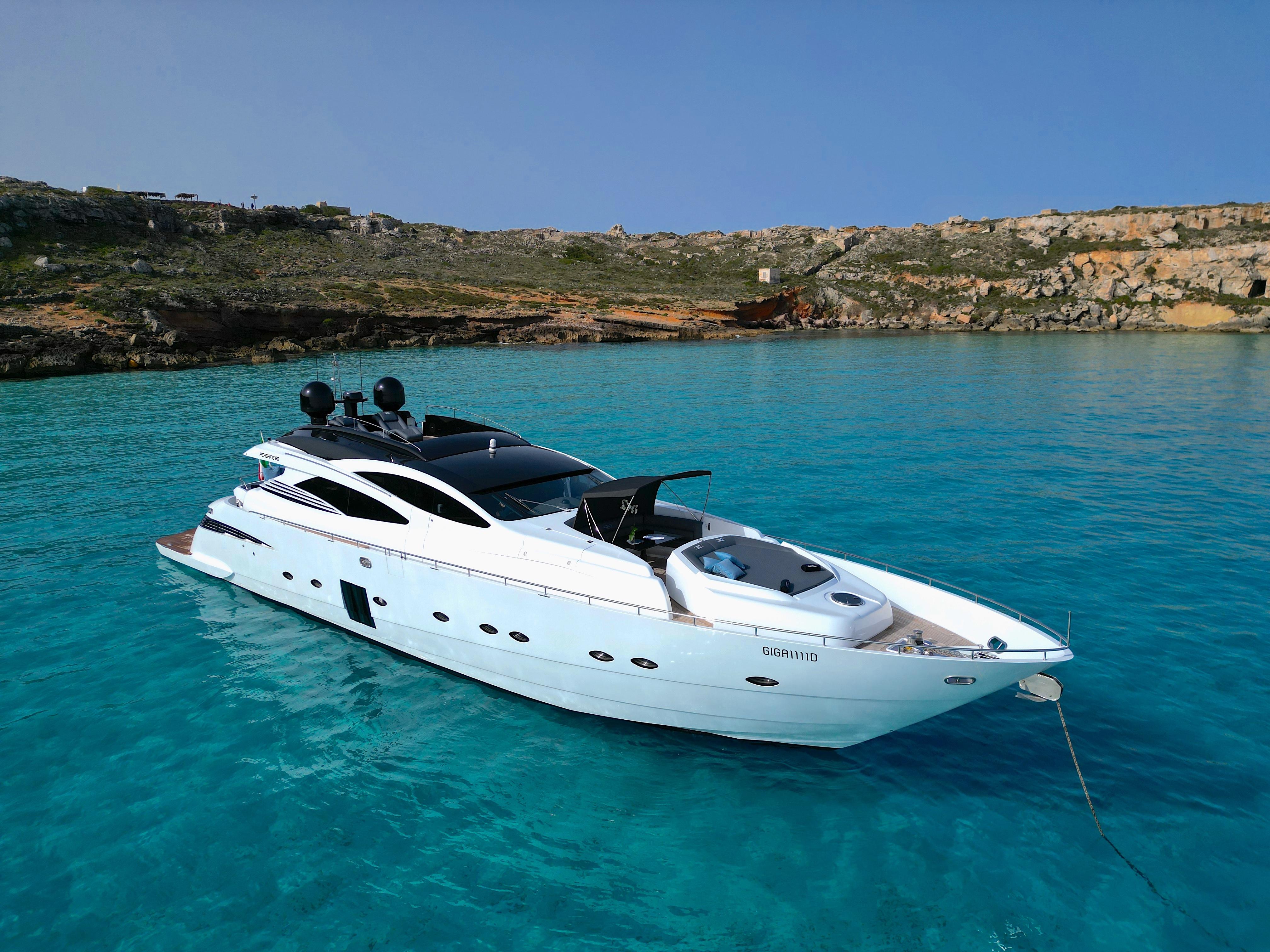 2008 Pershing 90 yacht anchored in clear turquoise waters near rocky coastline.