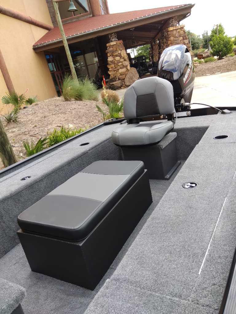 2025 Tracker Panfish 17 boat interior with seating and motor, parked near a rustic building.