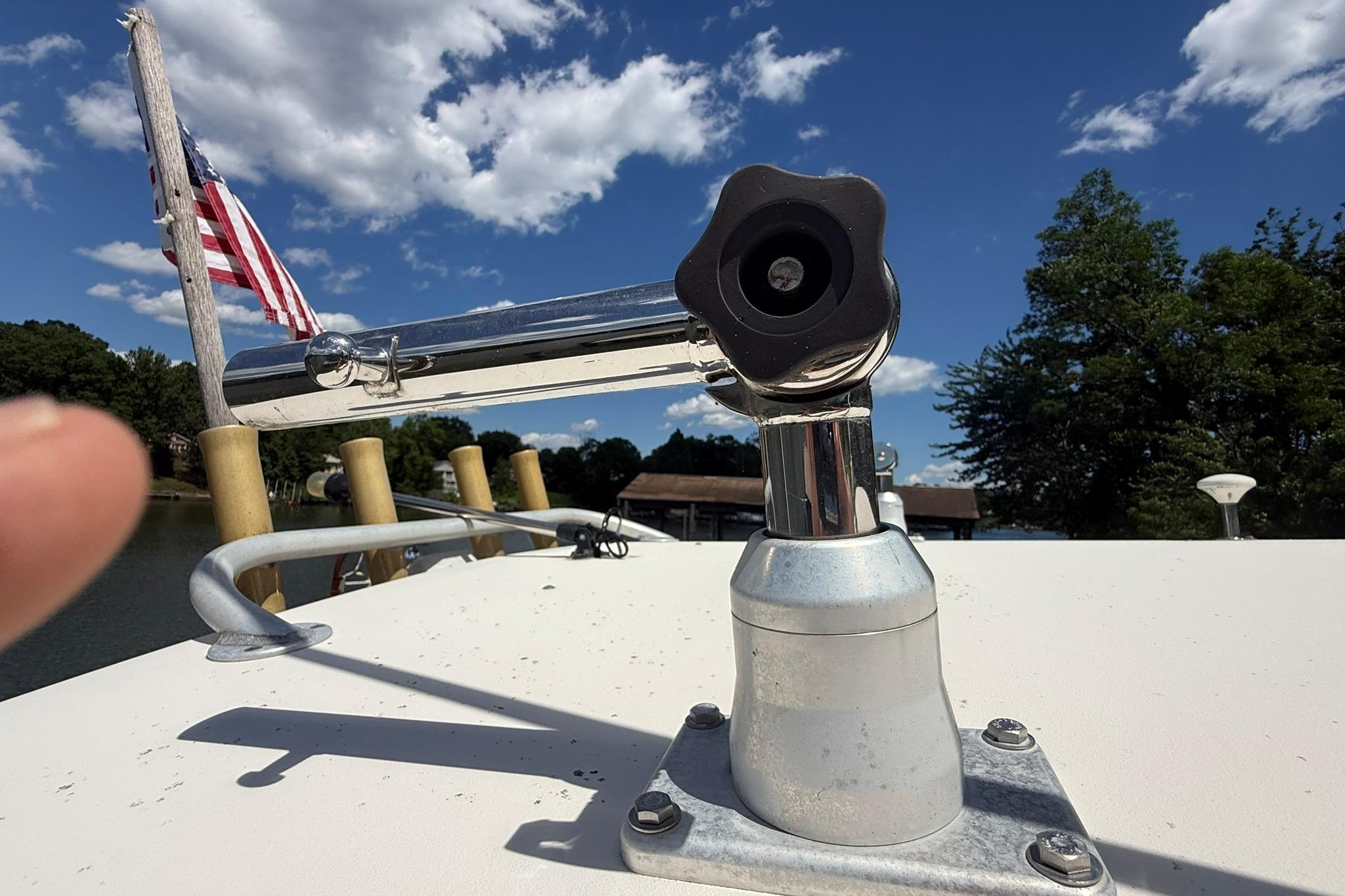 Boat deck with a metal fixture, American flag, and scenic lake view under blue sky.