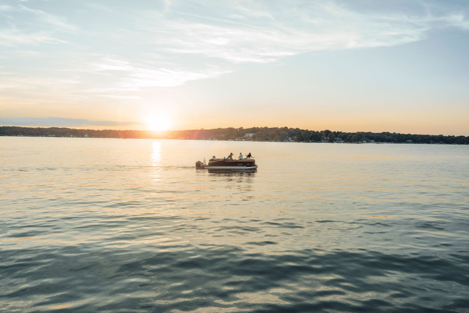A 2026 Harris Cruiser 230 on a calm lake at sunset.