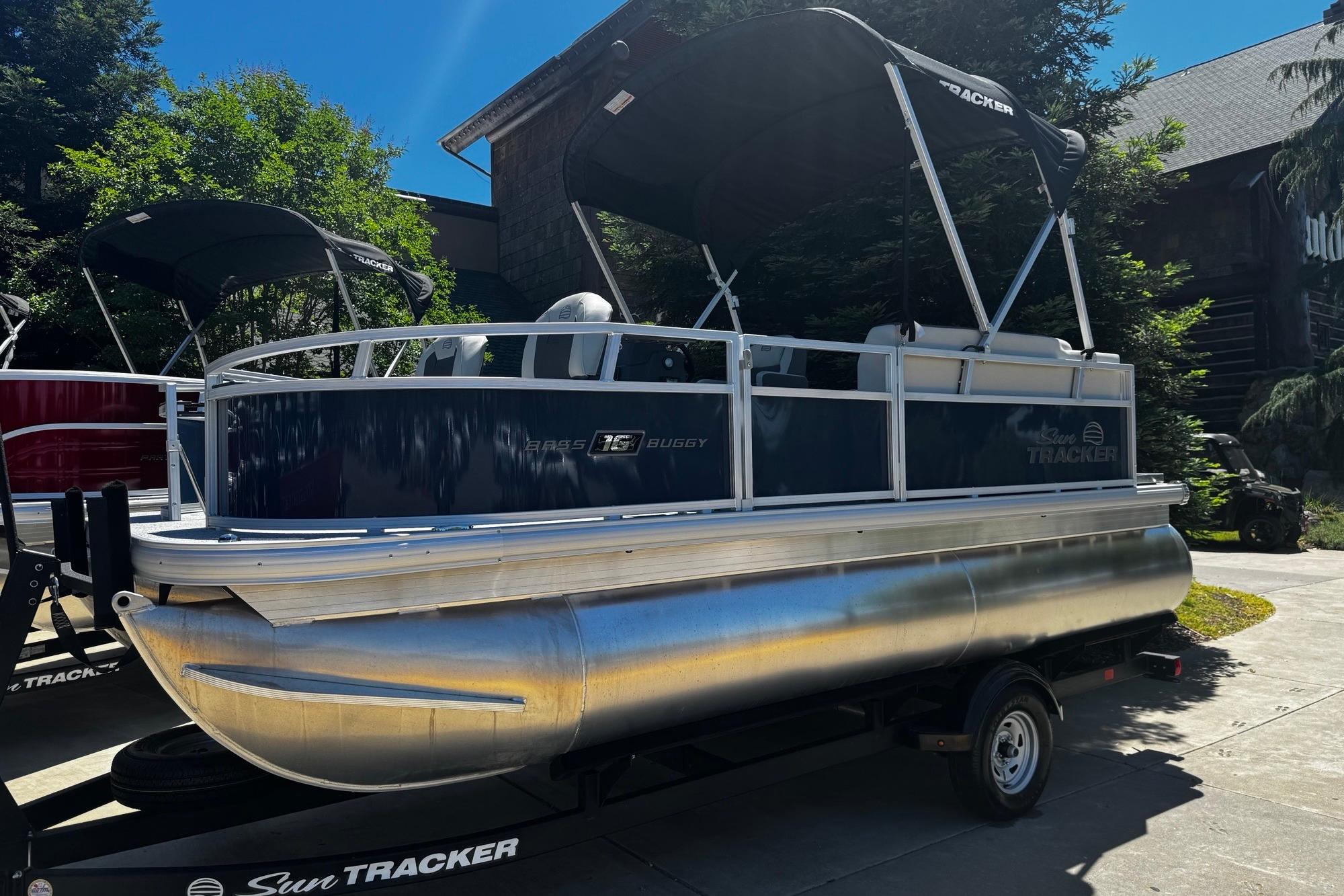 2026 Sun Tracker Bass Buggy 16 XL Select pontoon boat on trailer, parked outdoors.