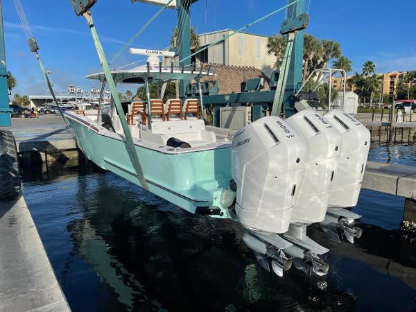 2025 Mag Bay 43 Center Console boat with triple outboard engines being lowered into water.