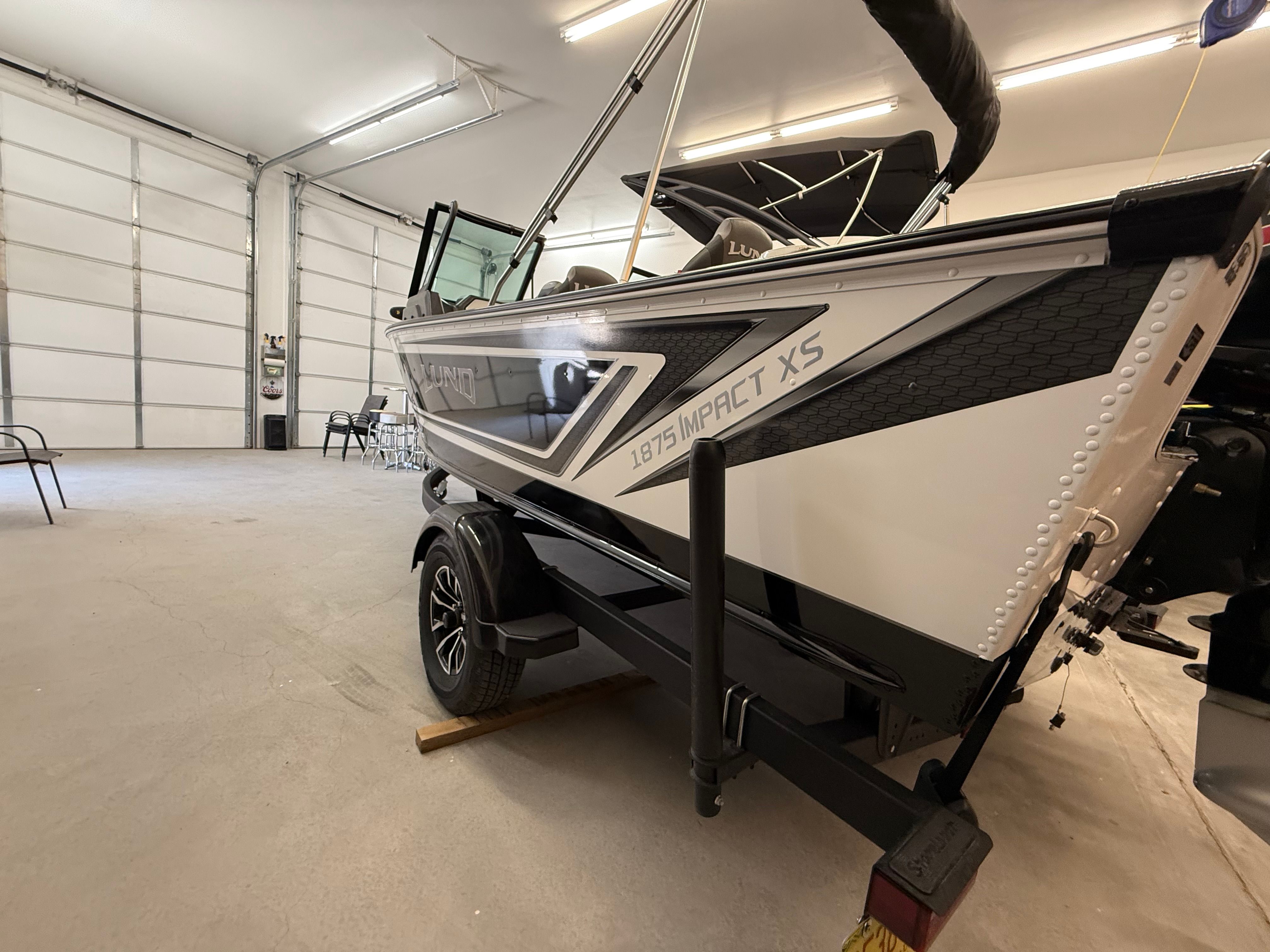 A 2025 Lund 1875 Impact XS Sport boat is in a garage on a trailer.